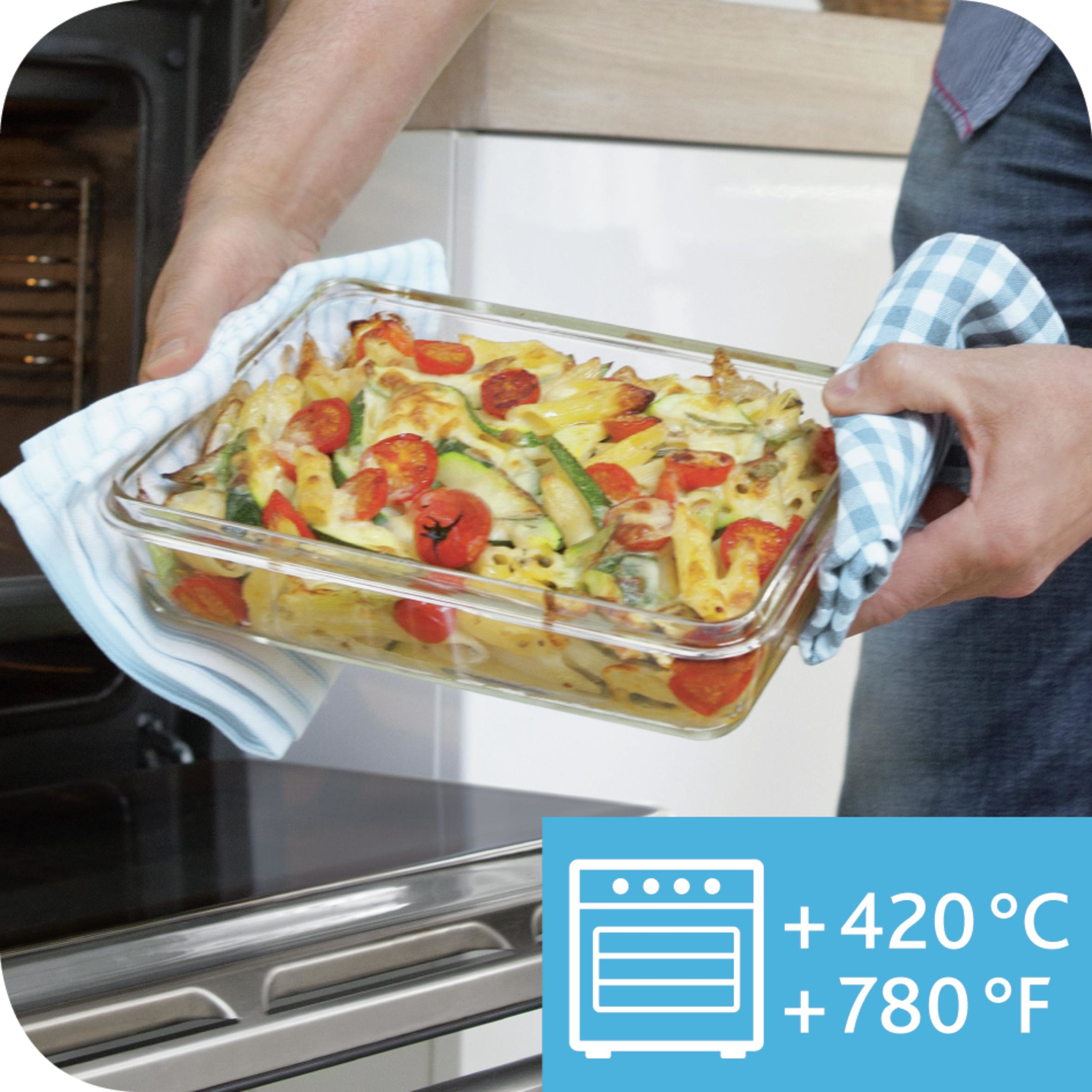 Una persona sostiene una fuente de vidrio con comida horneada, usando paños de cocina. La fuente está cerca de un horno.