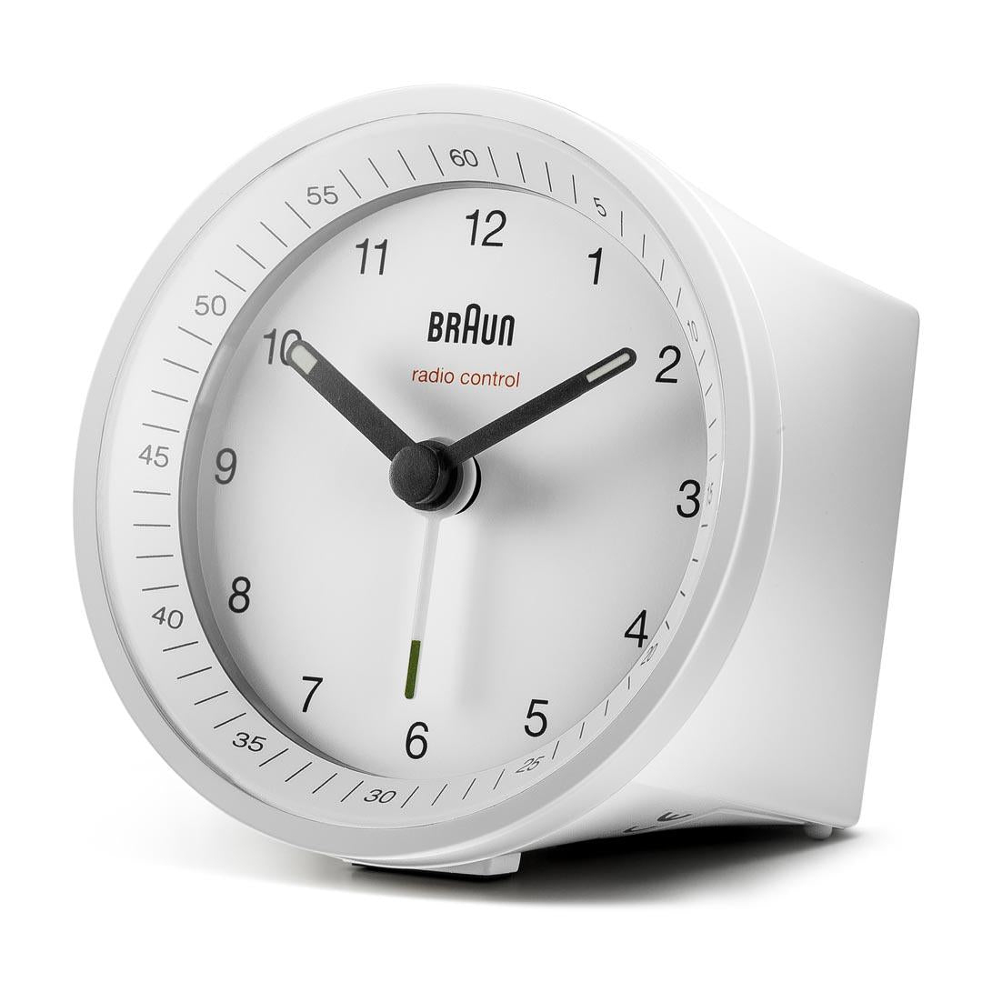 Un réveil Braun blanc radiocommandé. Les aiguilles noires indiquent l'heure. Les chiffres sont noirs sur un cadran blanc. La marque est visible.