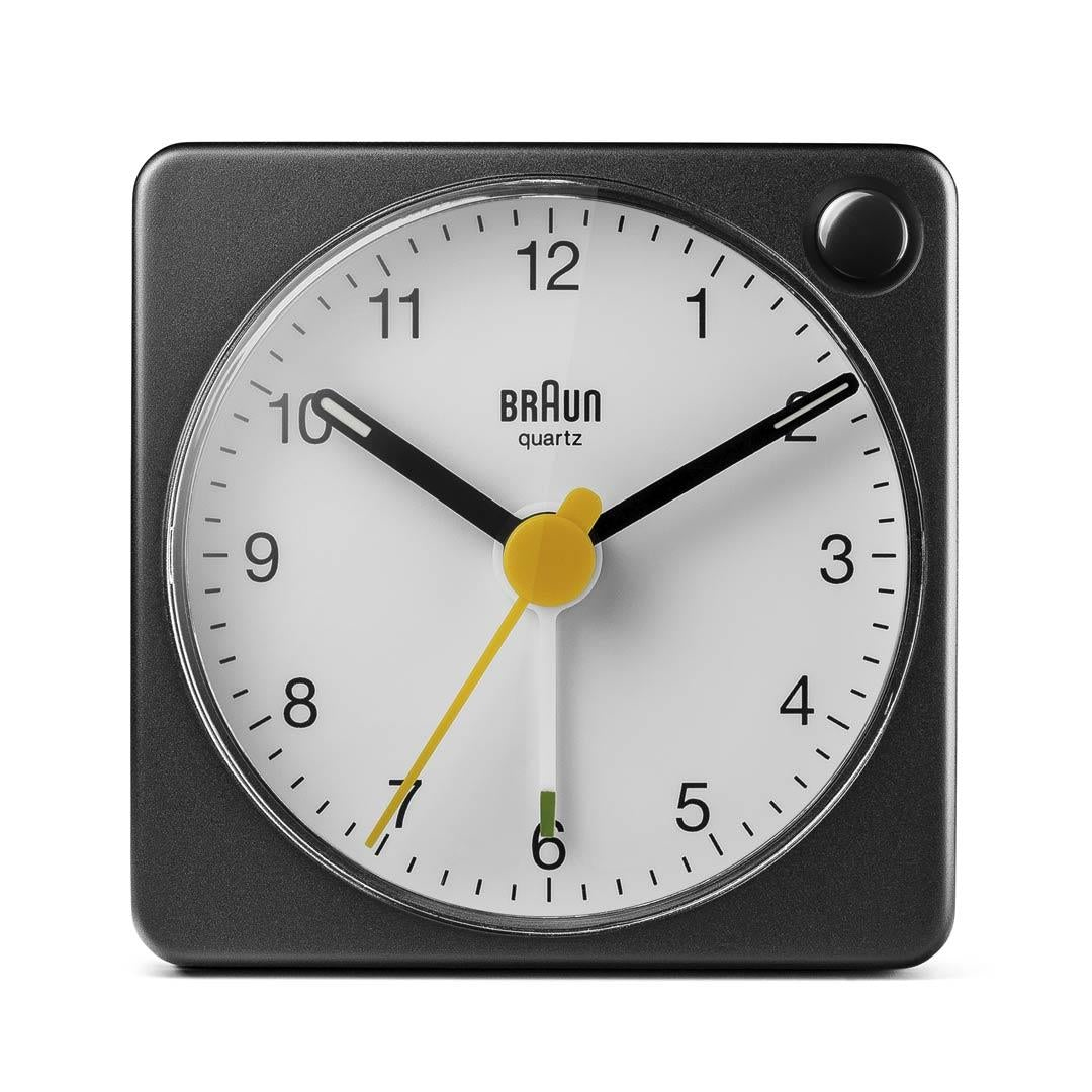 Un réveil Braun à quartz carré. Boîtier noir, cadran blanc avec chiffres et aiguilles noirs. Aiguille des secondes jaune. Il est 1h10.