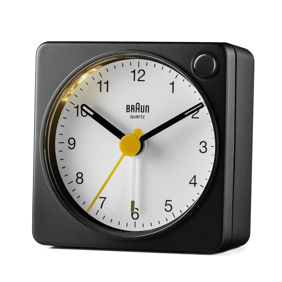 Un réveil à quartz Braun noir. Il a un cadran blanc, des aiguilles noires et une trotteuse jaune. L'horloge est carrée.