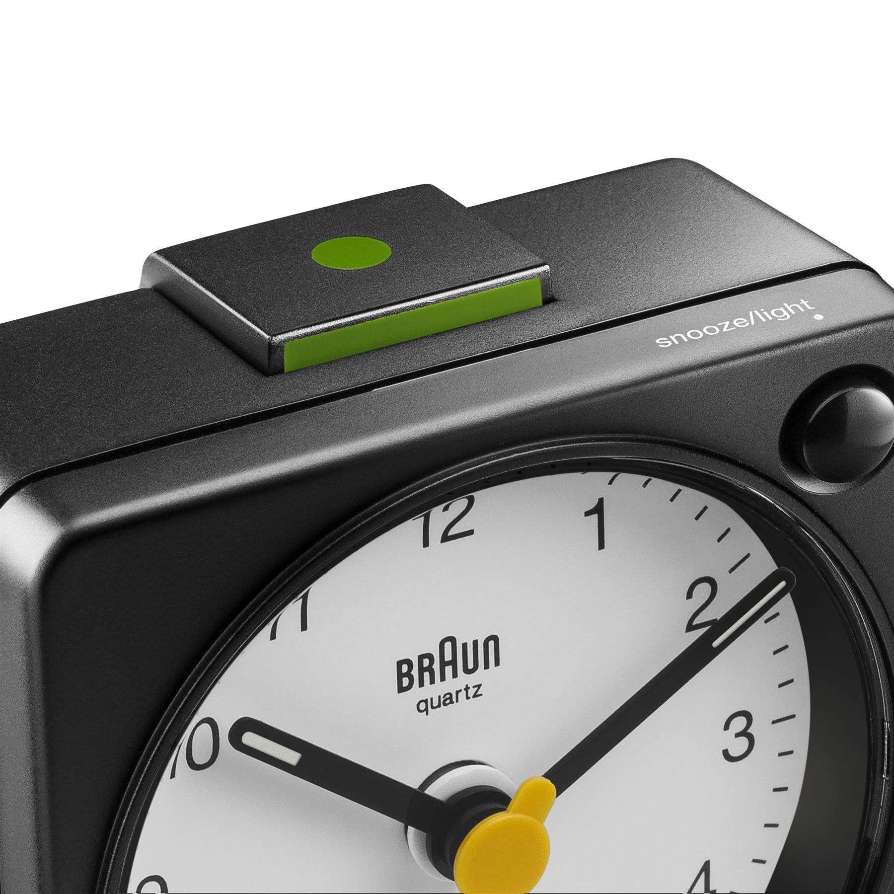 Un réveil Braun quartz noir. L'horloge a un cadran blanc, des aiguilles noires et un bouton de répétition jaune.