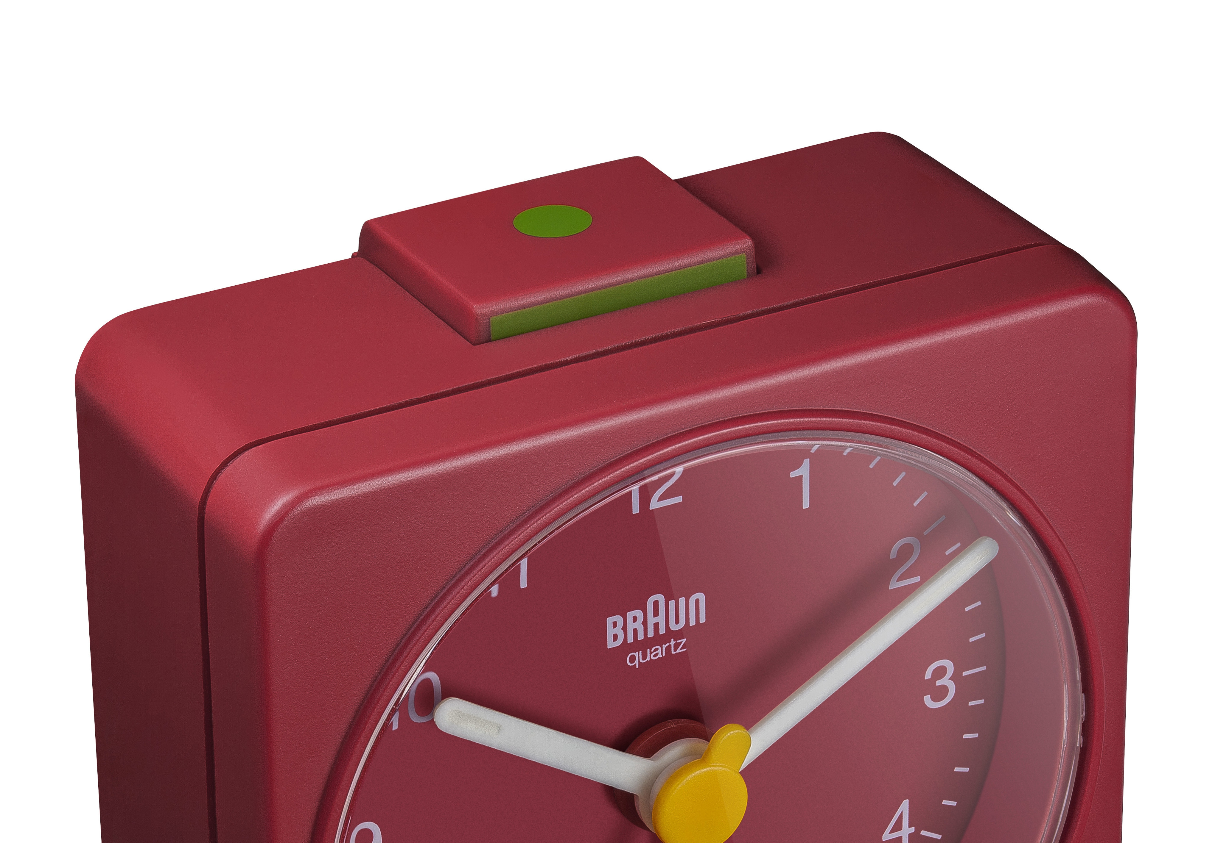 Un réveil Braun quartz rouge. Il a un bouton vert sur le dessus. Les aiguilles sont blanches.