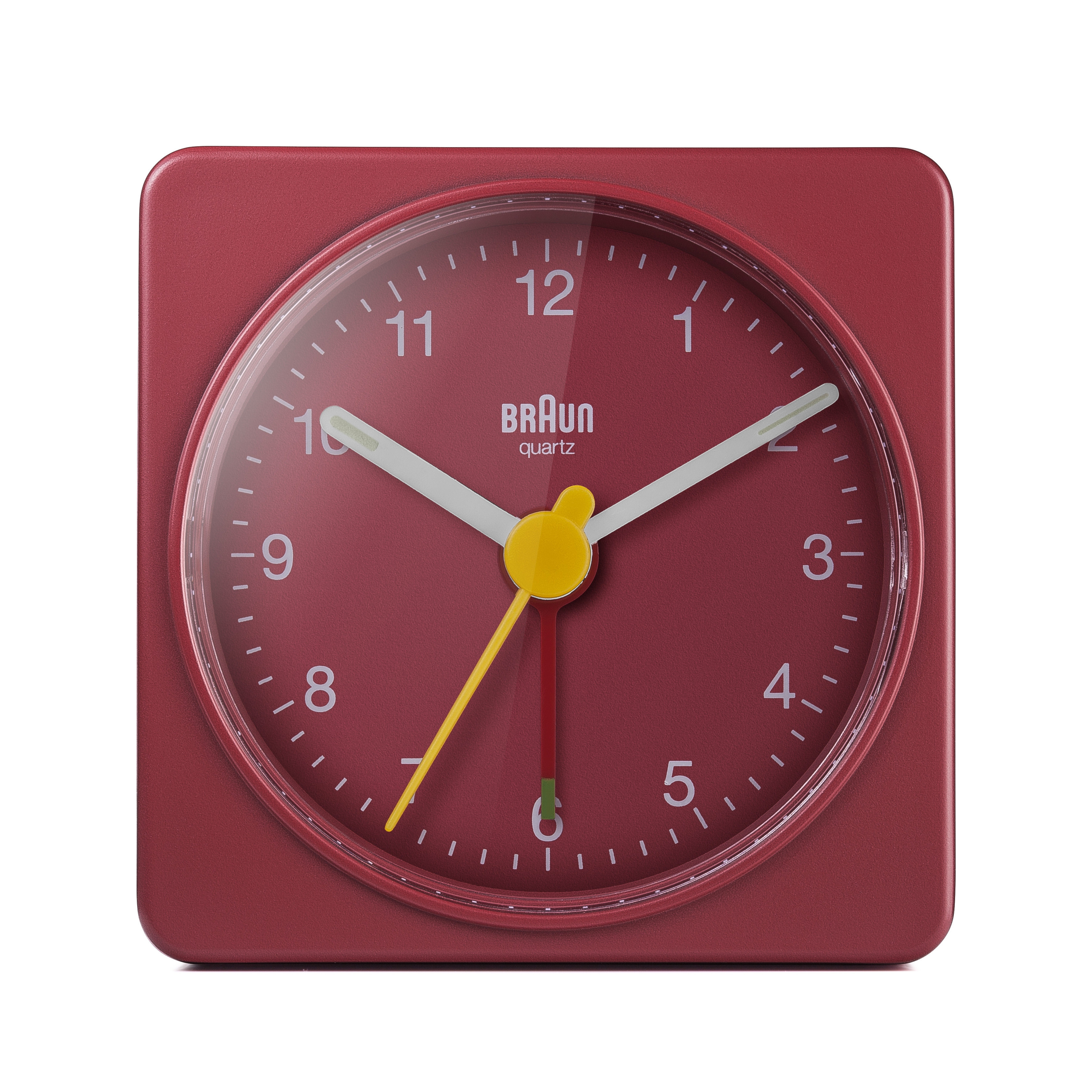 Un réveil Braun quartz rouge carré. Il a des chiffres, des aiguilles et un bouton jaune sur fond rouge.