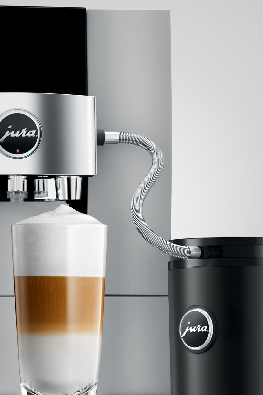 Una cafetera que dispensa un café con leche en capas en un vaso. La máquina es plateada y negra, con un logotipo de Jura.