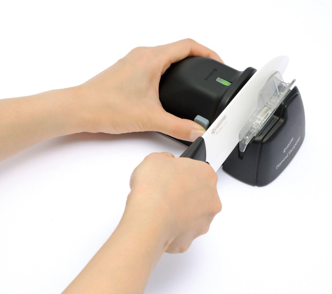 Eine Person schärft ein weißes Messer mit einem schwarzen Kyocera Diamantschärfer. Hände halten sowohl das Messer als auch den Schärfer.