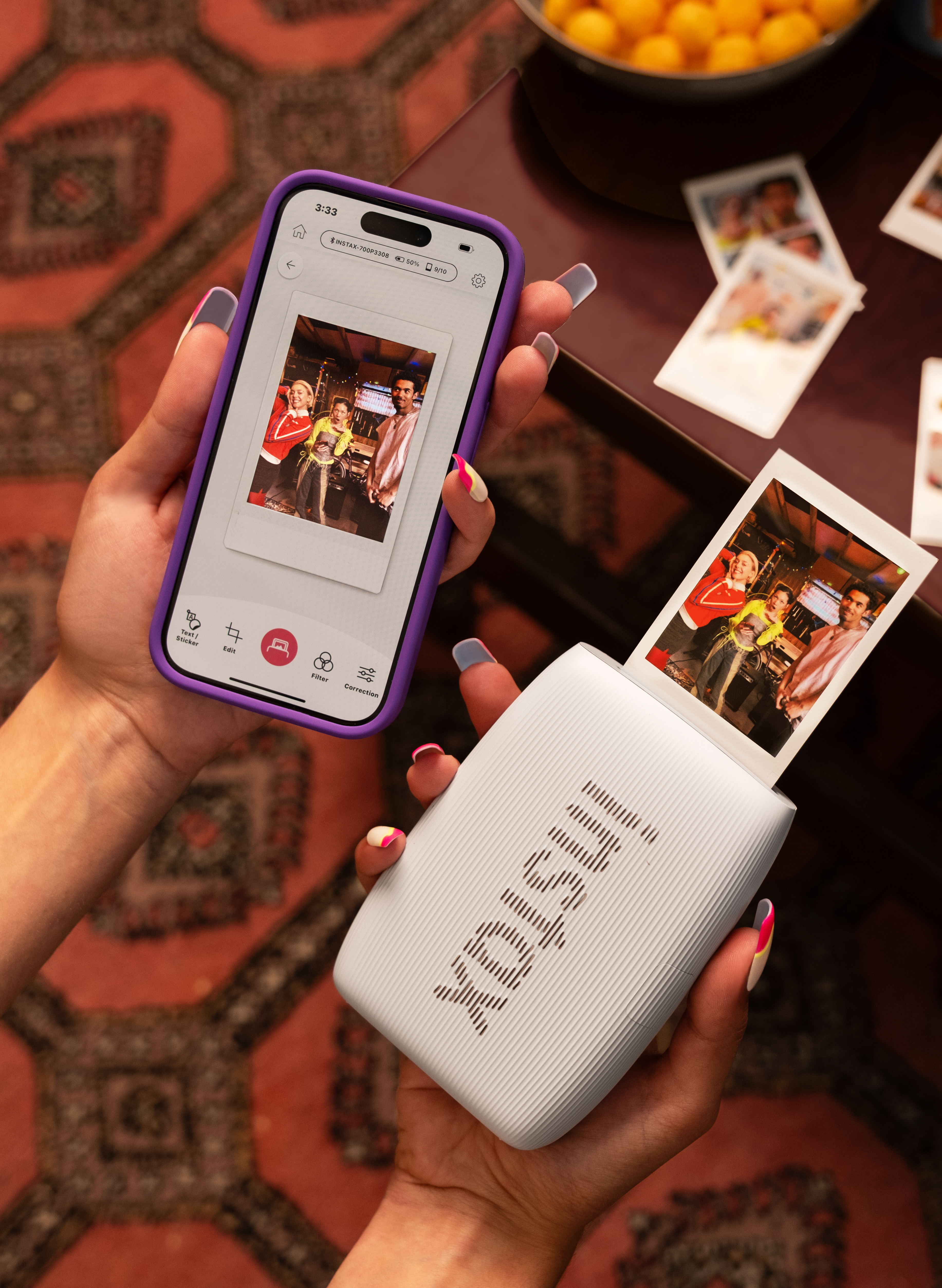 Eine Person hält ein Telefon und einen Drucker mit Fotos. Das Telefon zeigt ein Foto von drei Personen. Ein gedrucktes Foto erscheint.