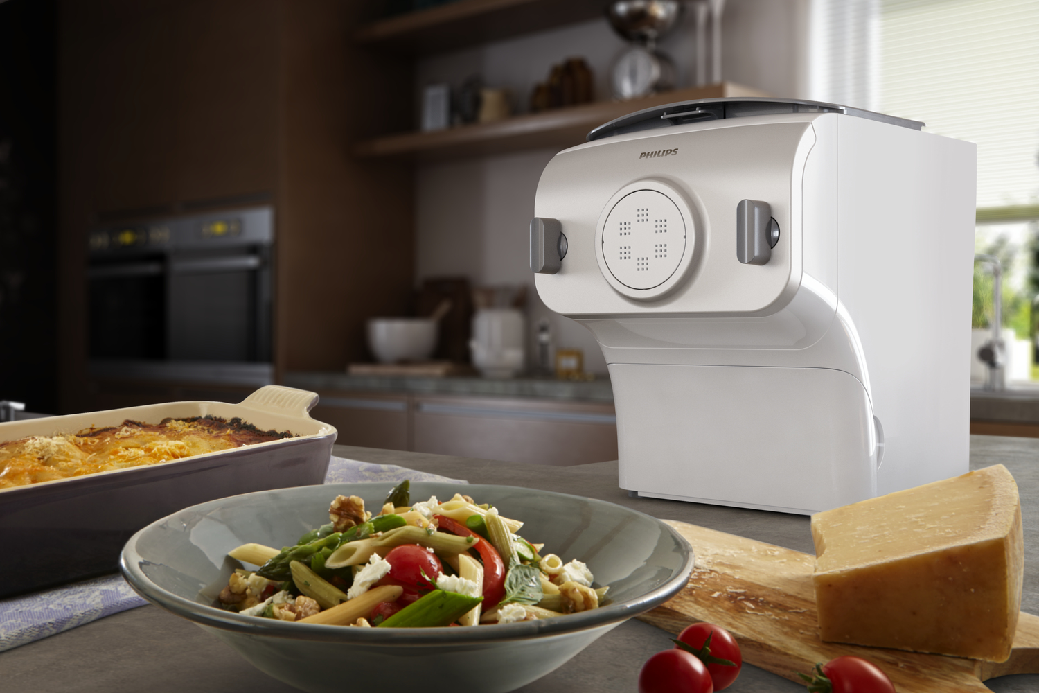 Nudelmaschine mit Pasta, Käse und Tomaten auf einem Holzbrett. Ein Auflauf befindet sich im Hintergrund.
