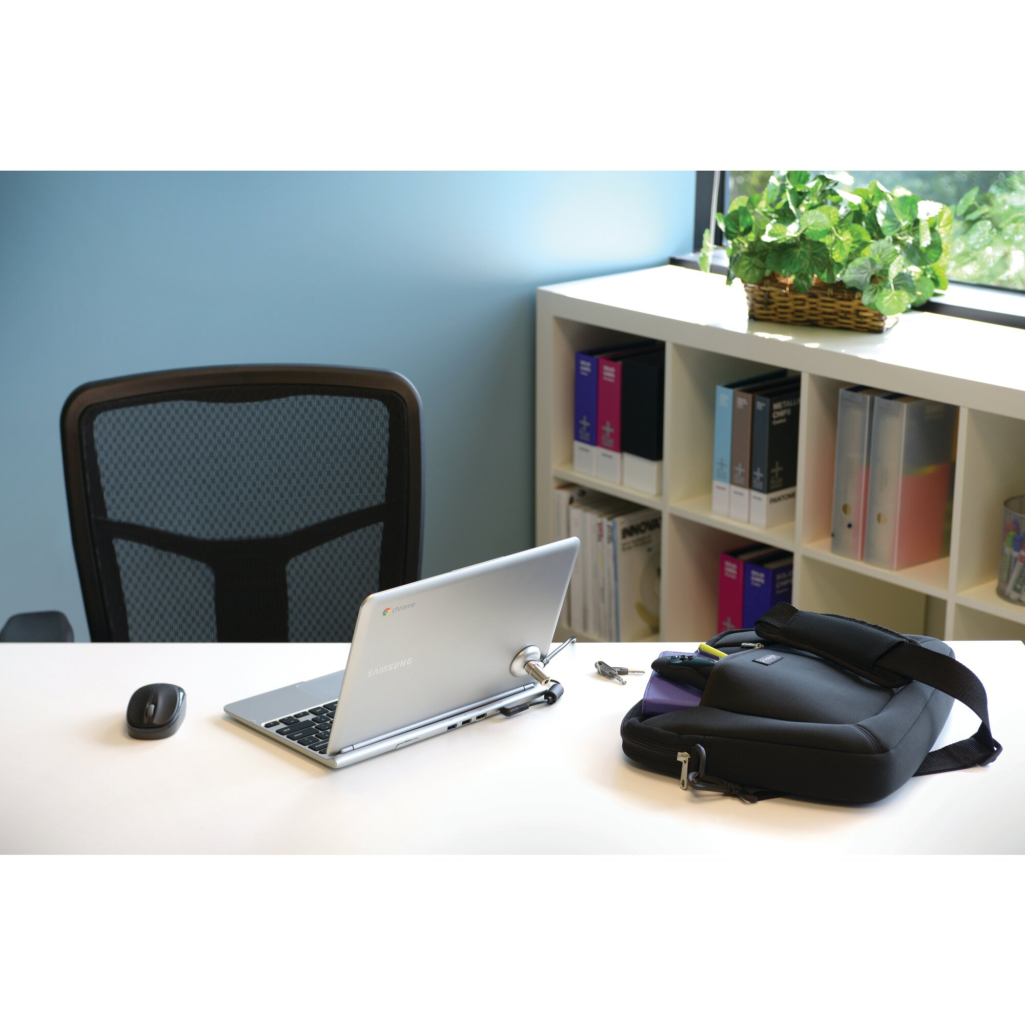 Ein Laptop mit Schloss, Maus, Tasche und Schlüsseln auf einem weißen Schreibtisch. Ein schwarzer Bürostuhl steht dahinter.