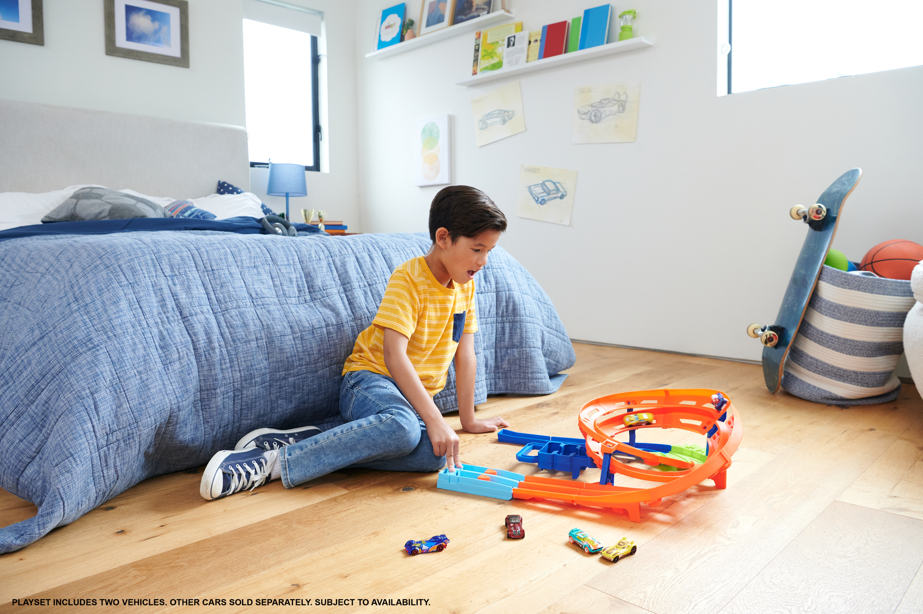 Chłopiec bawi się zestawem torów dla zabawek. W tle łóżko, deskorolka i zabawki.