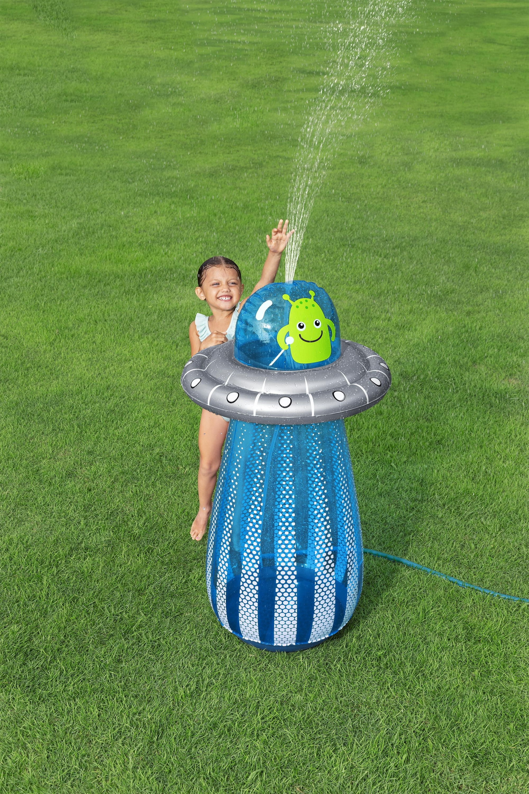 Dziewczynka bawi się w wodzie z kosmicznego zraszacza na zielonej trawie.
