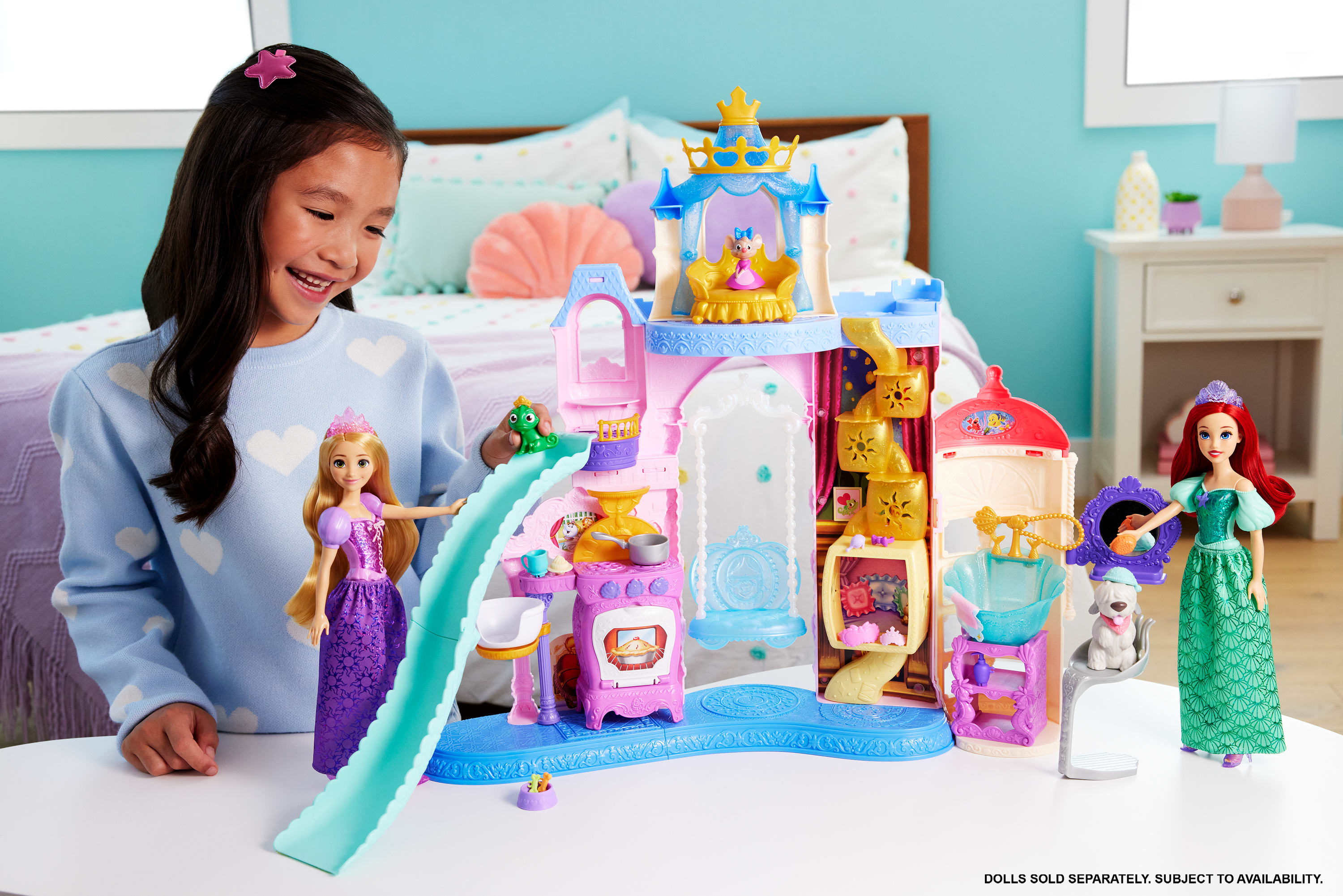 Una niña juega con un juguete de castillo de princesas de Disney. Hay muñecas de Rapunzel y Ariel. El fondo es un dormitorio.