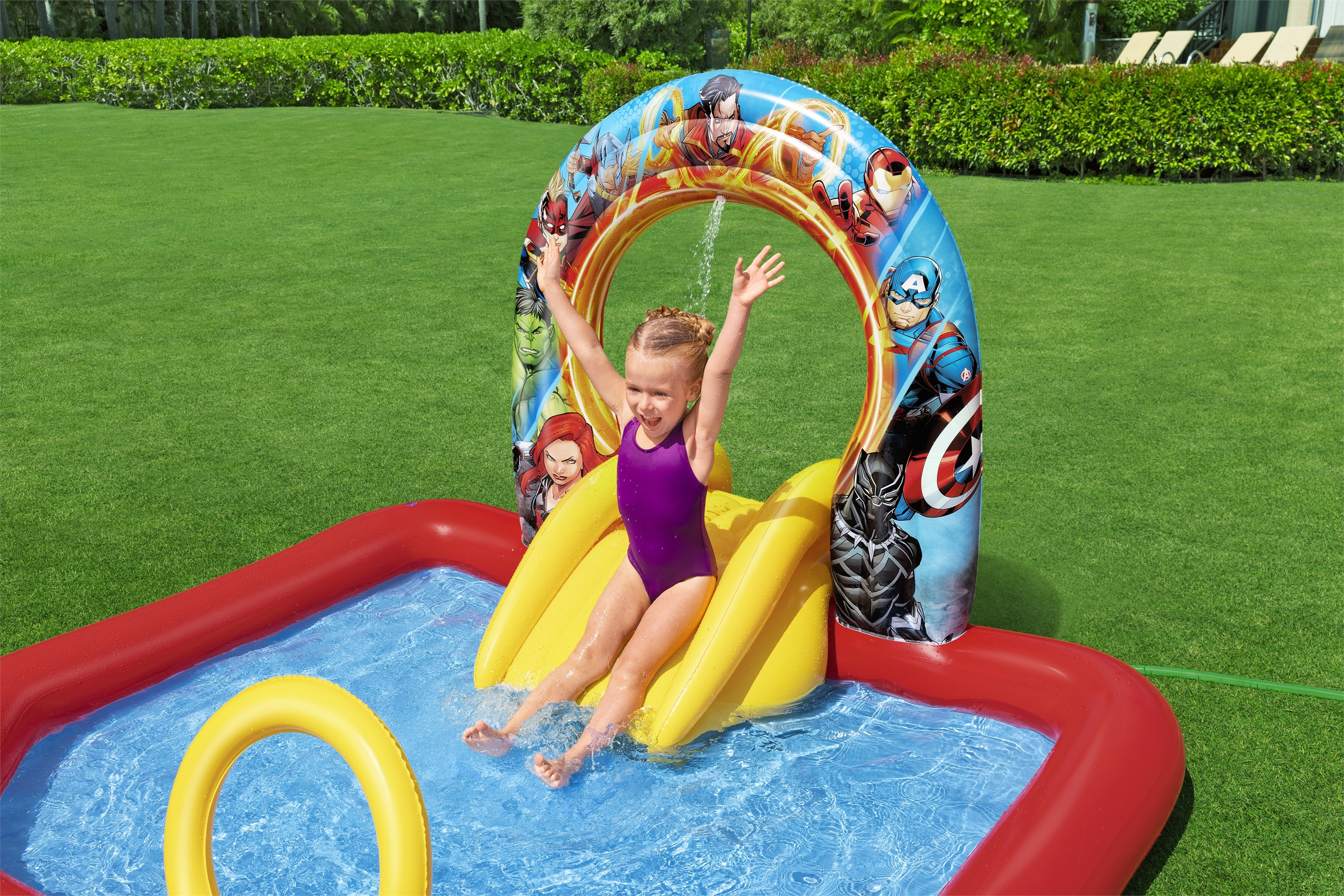 Dziewczyna w fioletowym stroju kąpielowym zjeżdża z żółtej zjeżdżalni do basenu. Postacie Marvela są na łuku.