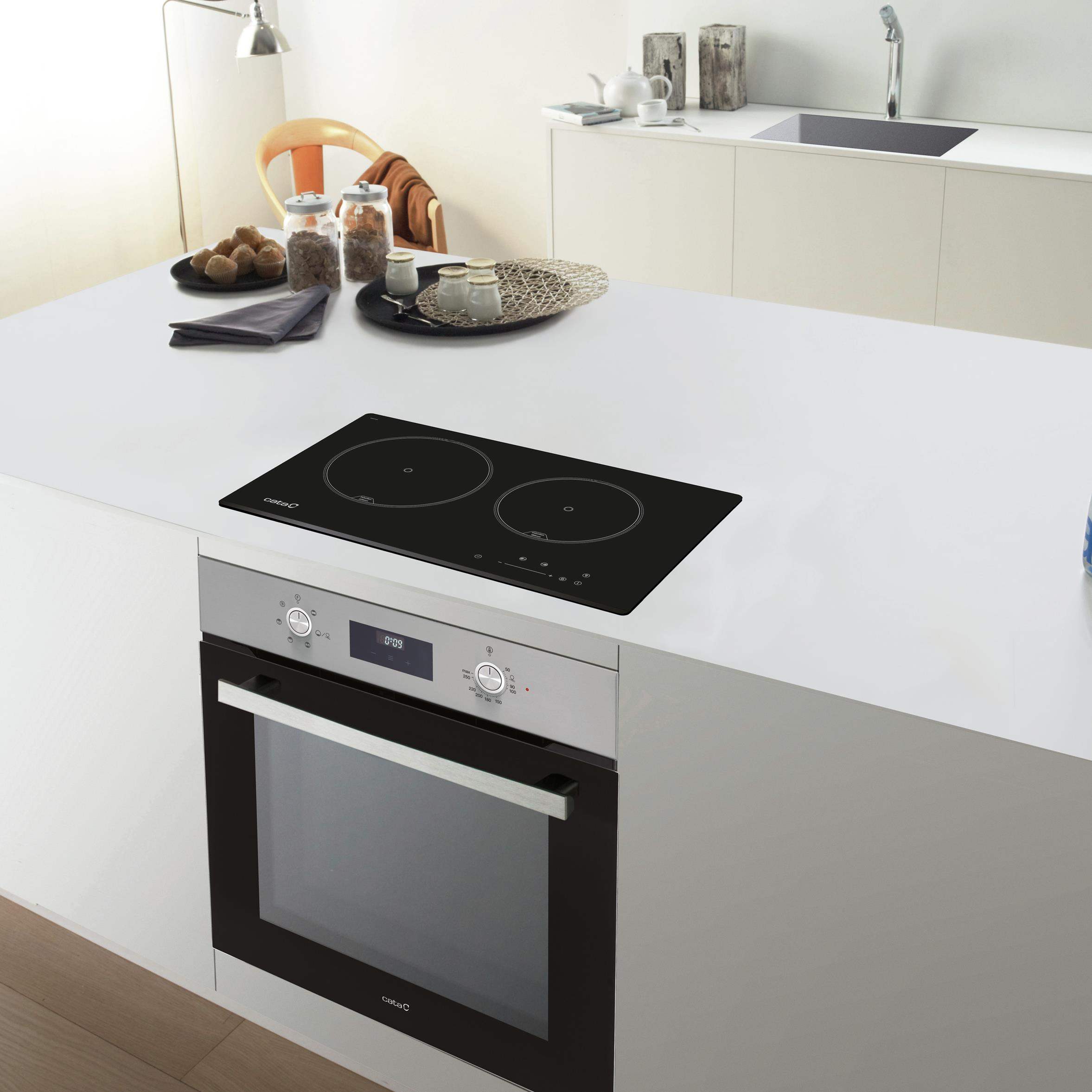 Un'isola cucina moderna con piano cottura a induzione e forno. Vari oggetti sul bancone.