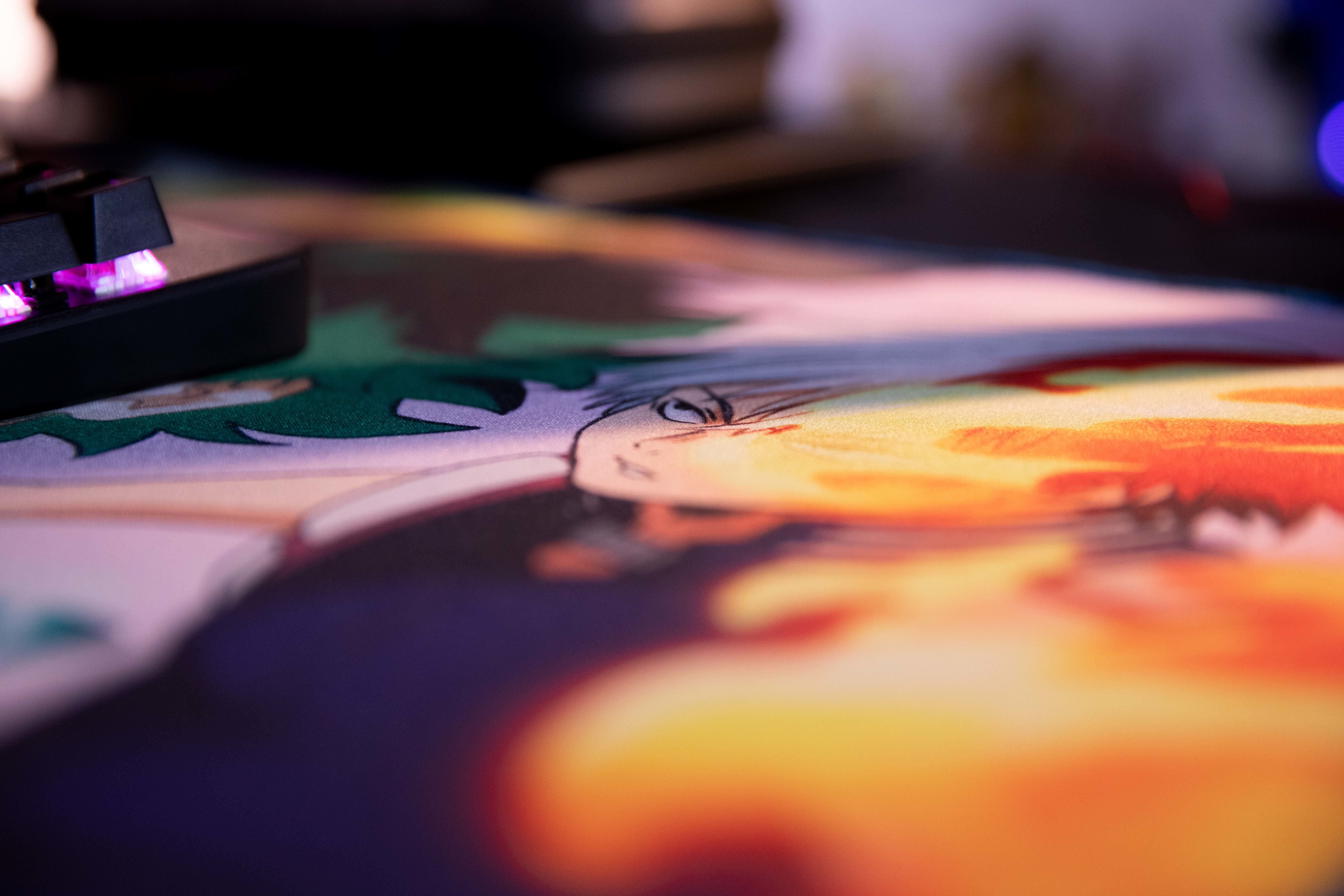 Zbliżenie pokazuje klawiaturę i kolorową podkładkę pod mysz z projektem postaci. Klawisze klawiatury mają fioletowe światła.