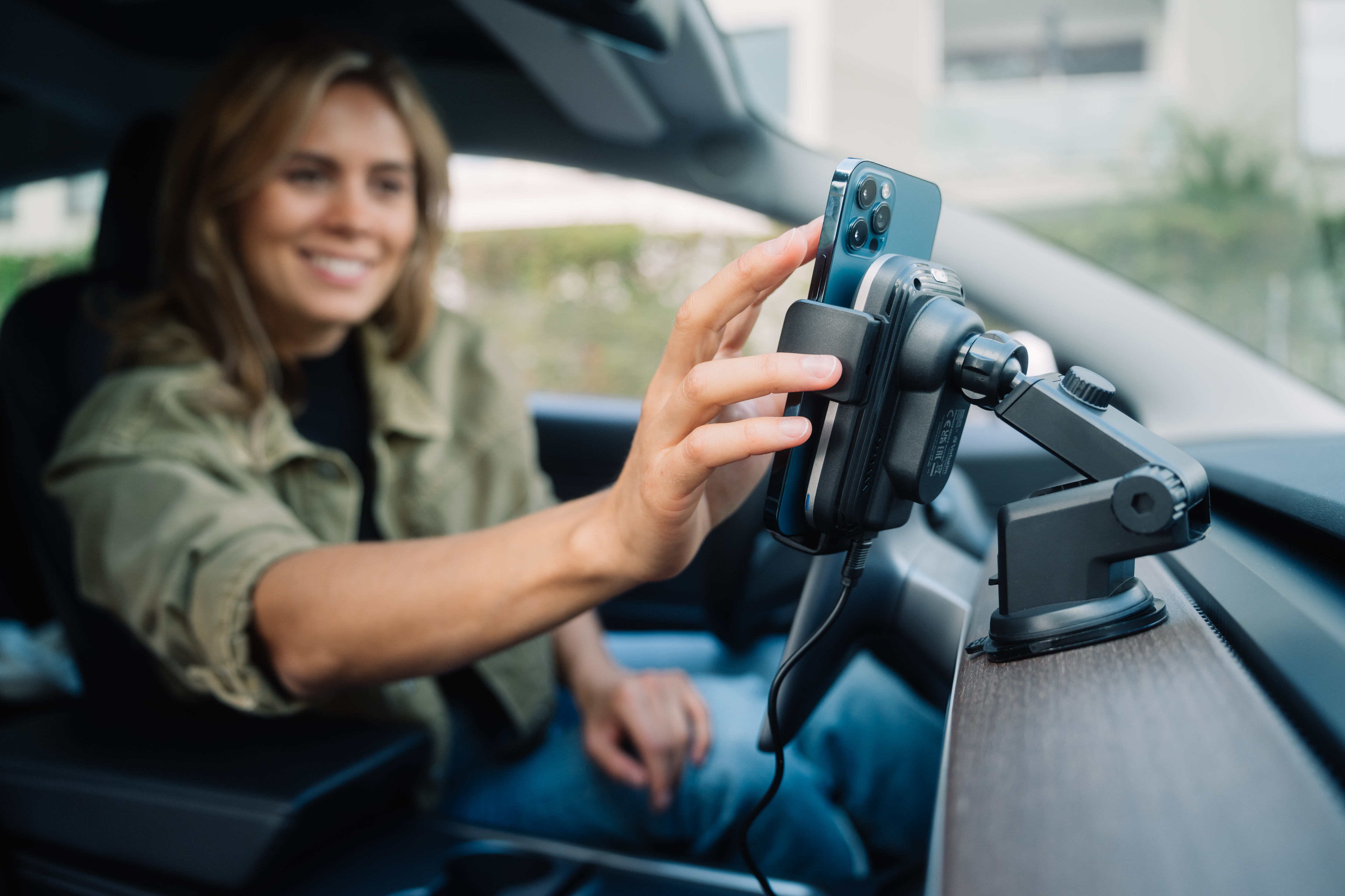 Una mujer en un coche inserta un teléfono en un soporte para coche. El teléfono es azul. La mujer está sonriendo.