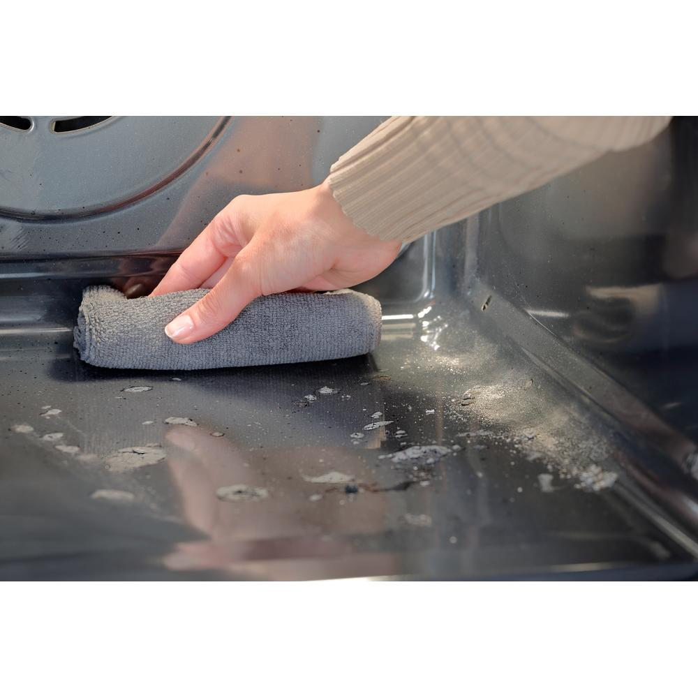 Una mano con un paño gris limpia el interior de un horno sucio. El horno está oscuro con manchas y residuos visibles.