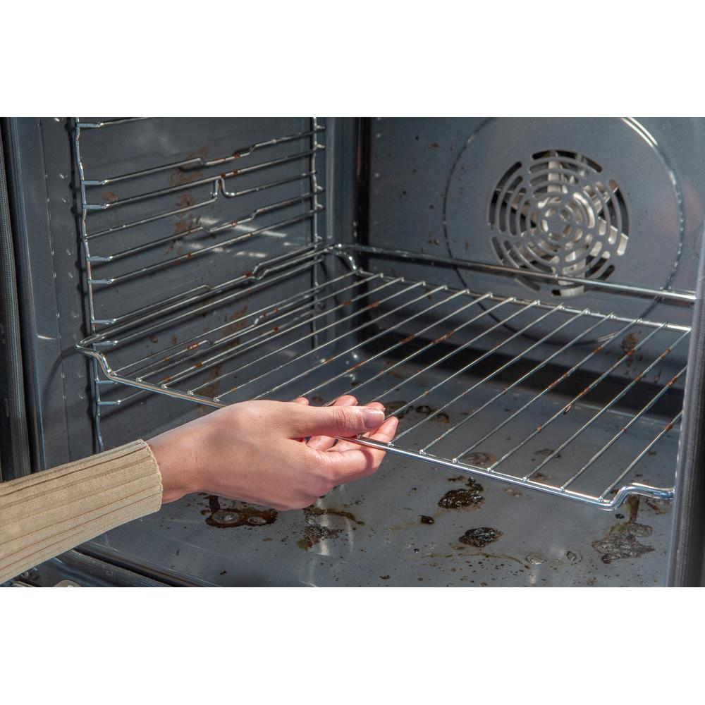 Una mano ajusta una rejilla de horno dentro de un horno sucio. El horno está abierto, y el fondo muestra un ventilador y el interior del horno.
