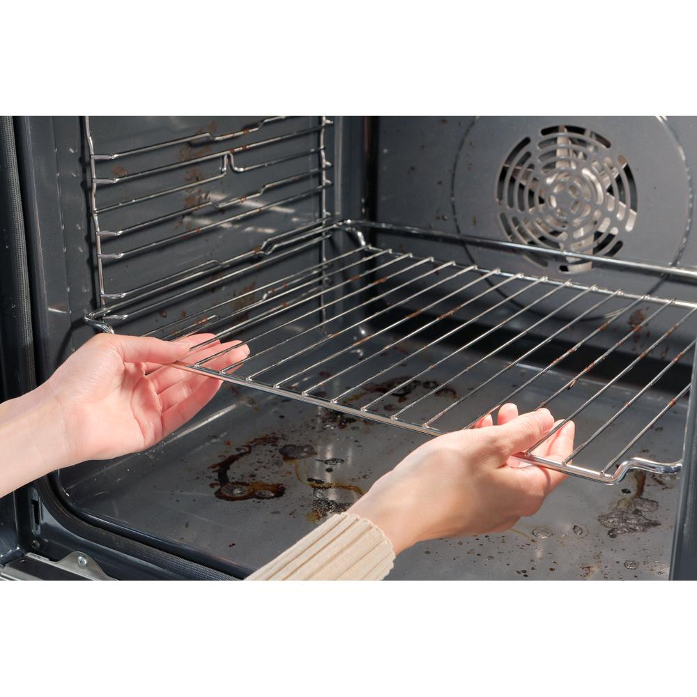 Unas manos colocan una rejilla cromada dentro de un horno sucio. El interior del horno es oscuro y tiene un ventilador en la pared trasera.