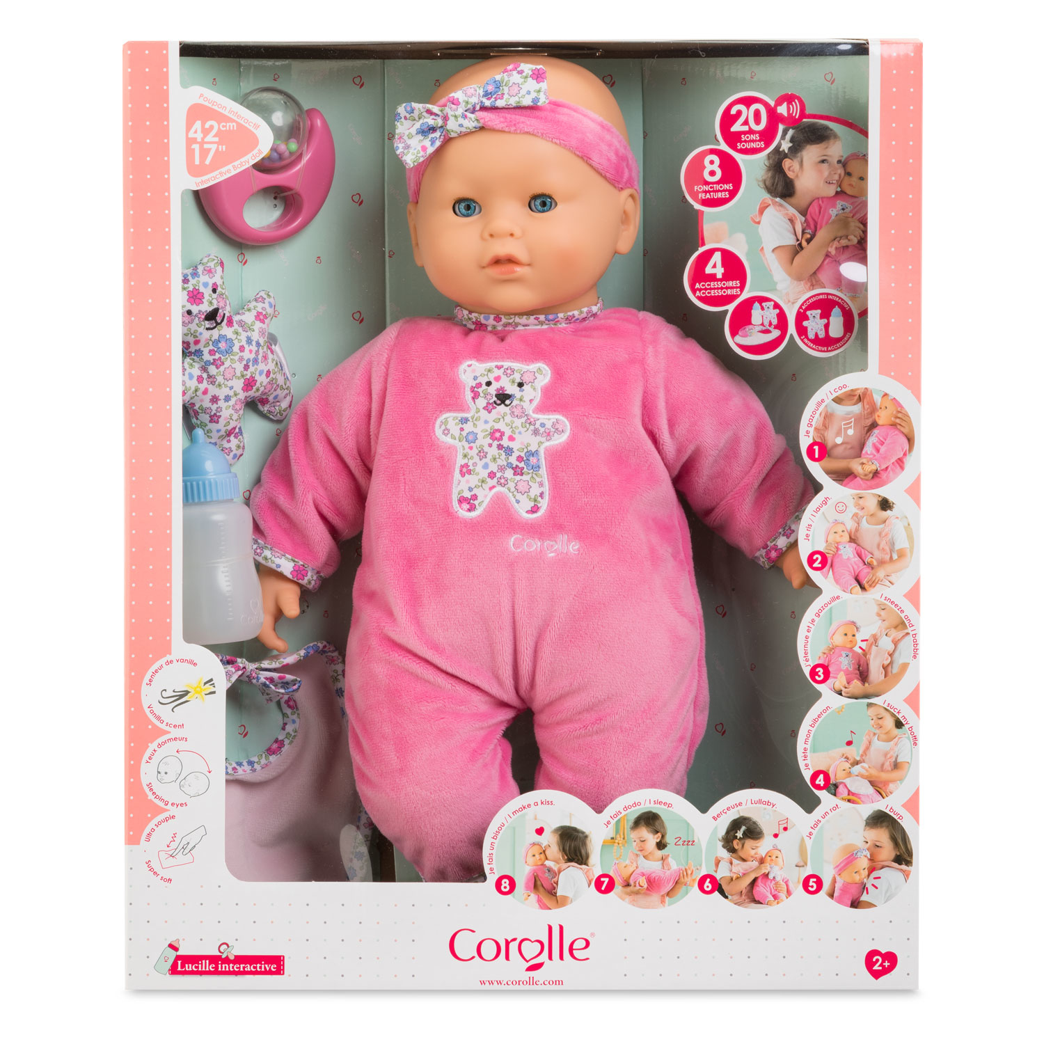 Eine Babypuppe in einer Box, die einen rosa Anzug trägt. Zubehör sind eine Flasche, ein Schnuller und ein Plüschbär.
