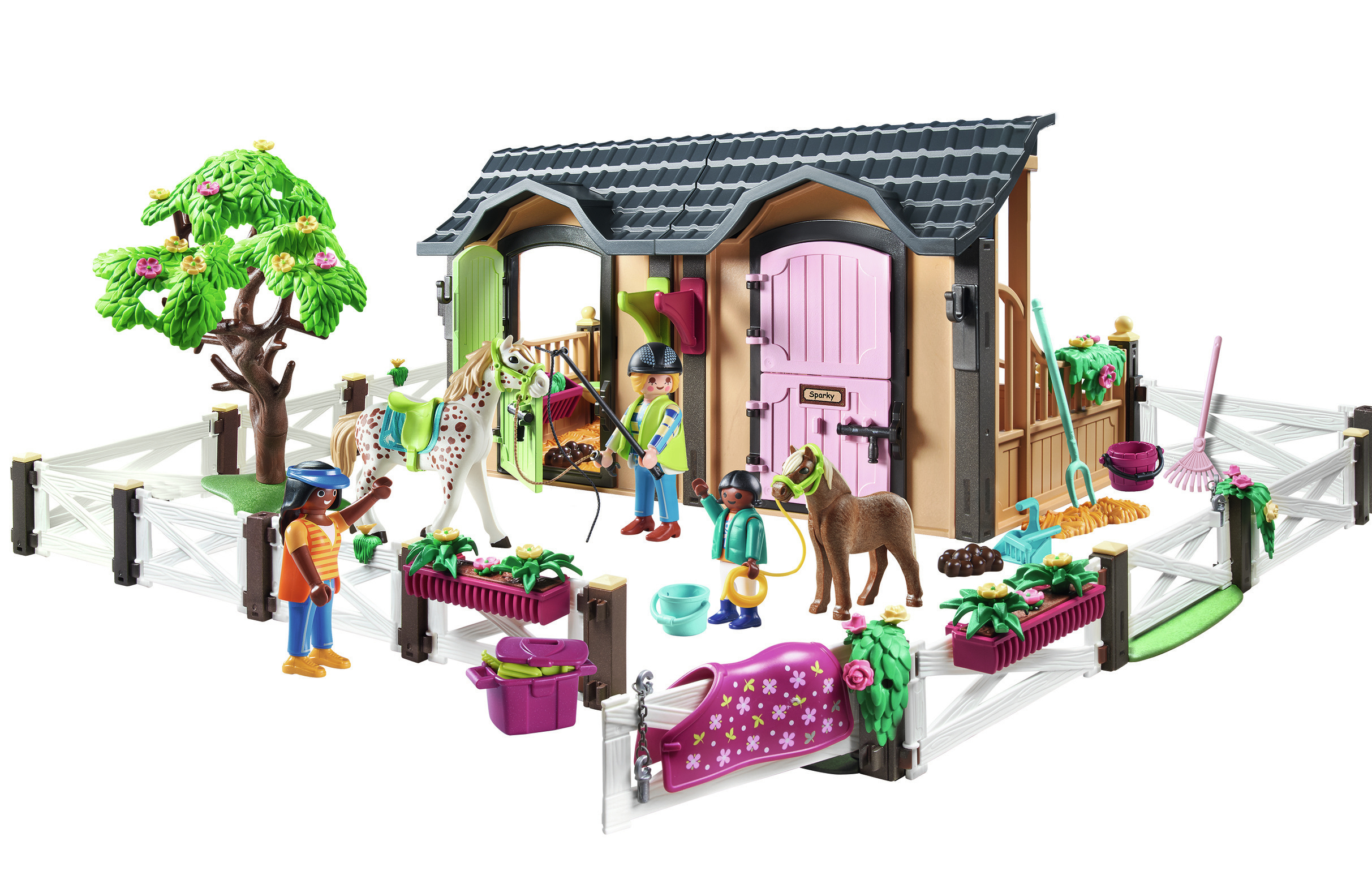 Une scène d'écurie de chevaux jouet avec des chevaux, des figurines, des outils et un arbre. L'écurie a des portes roses et un toit sombre.