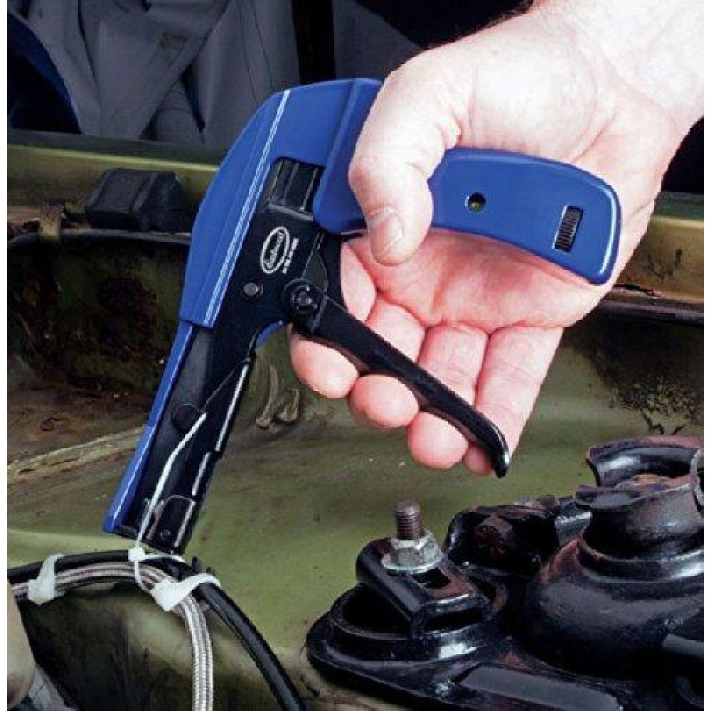 Una mano sostiene una herramienta azul y negra para bridas, usándola para apretar una brida blanca en cables negros, en un compartimento del motor.