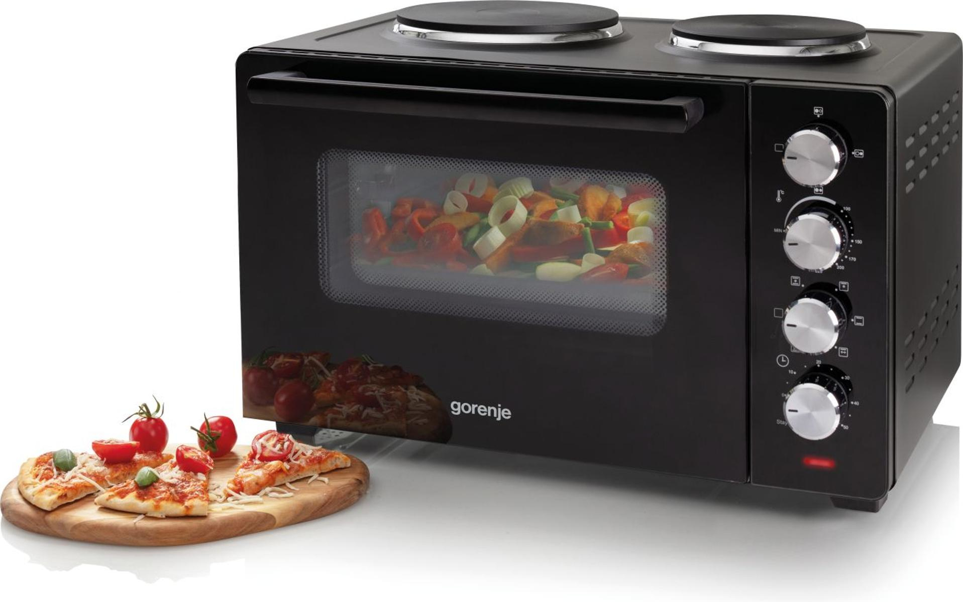 Schwarzer Ofen mit Pizza und Gemüse. Pizzen auf Holzbrett. Tomaten und Ofenbedienelemente sind sichtbar.