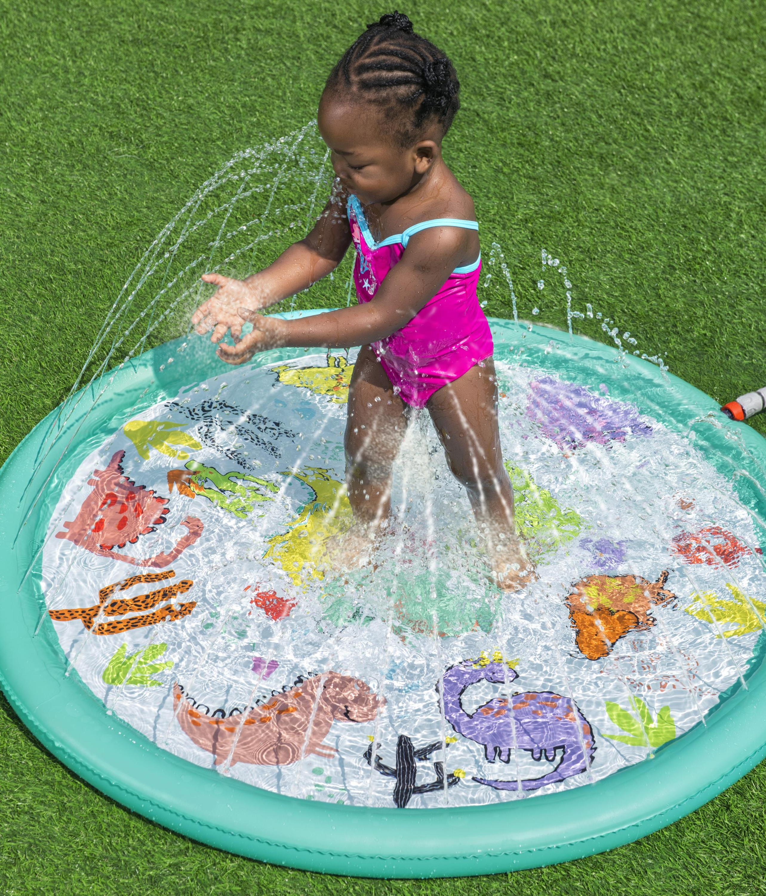 Una bambina in costume da bagno rosa gioca in una piscina per bambini a tema dinosauri sull'erba verde.