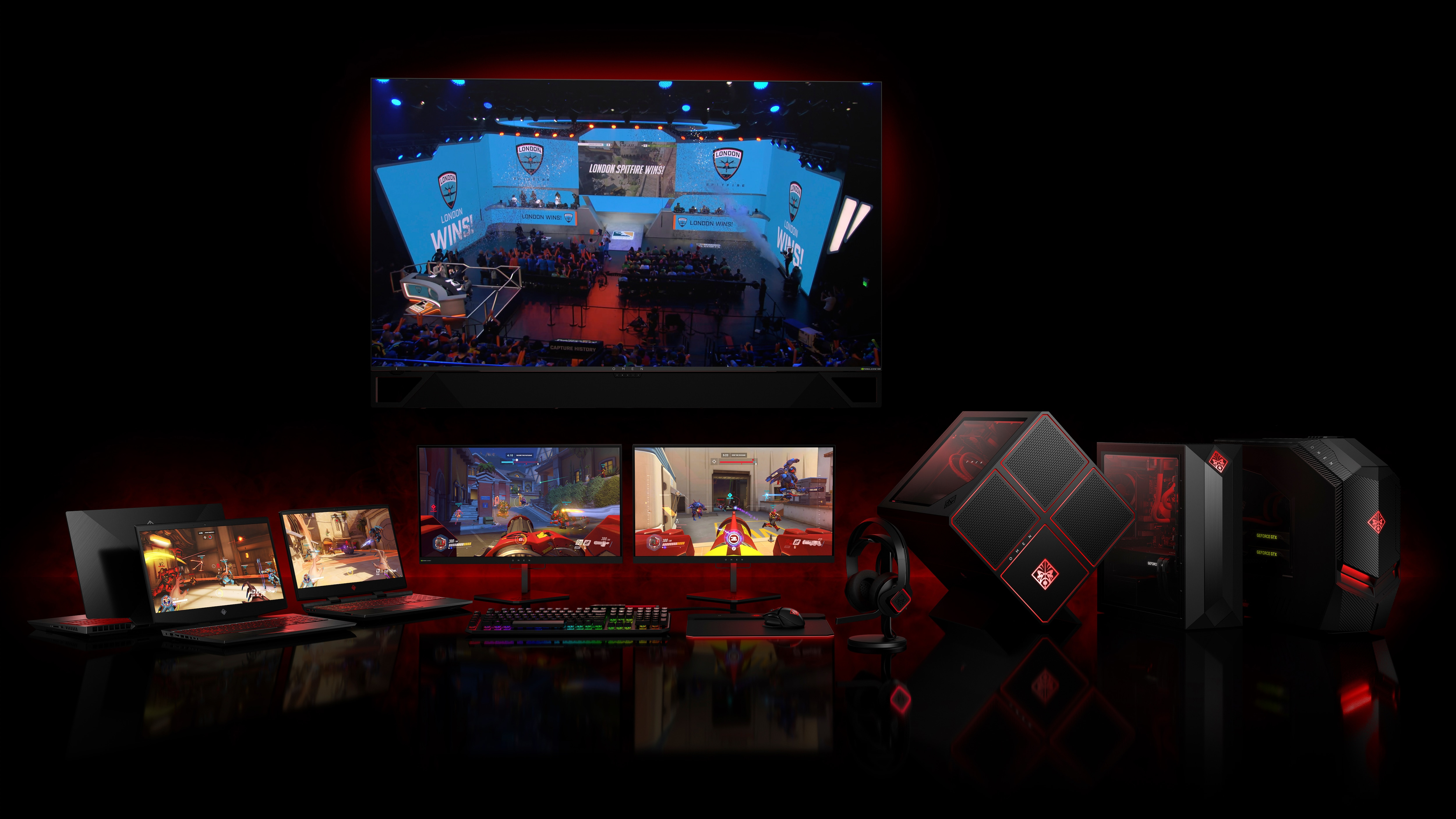 Konfiguracja do gier z wieloma ekranami wyświetlającymi grę, laptopami, komputerami do gier i akcesoriami na ciemnoczerwonym tle.