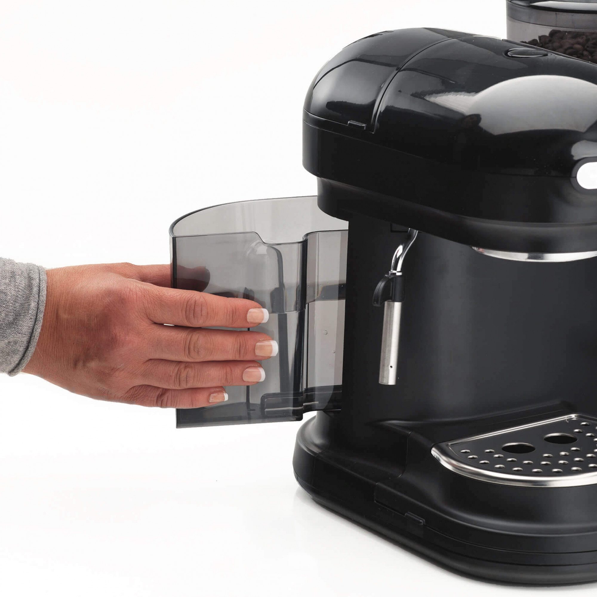 Ręka wkłada zbiornik na wodę do czarnego ekspresu do kawy. Maszyna stoi na białej powierzchni.