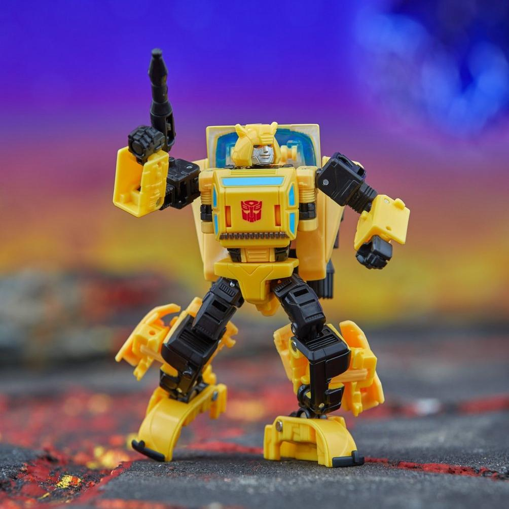 Una figura gialla di Bumblebee Transformer è in piedi con un braccio alzato. Ha dettagli neri e un simbolo Autobot rosso sul petto.