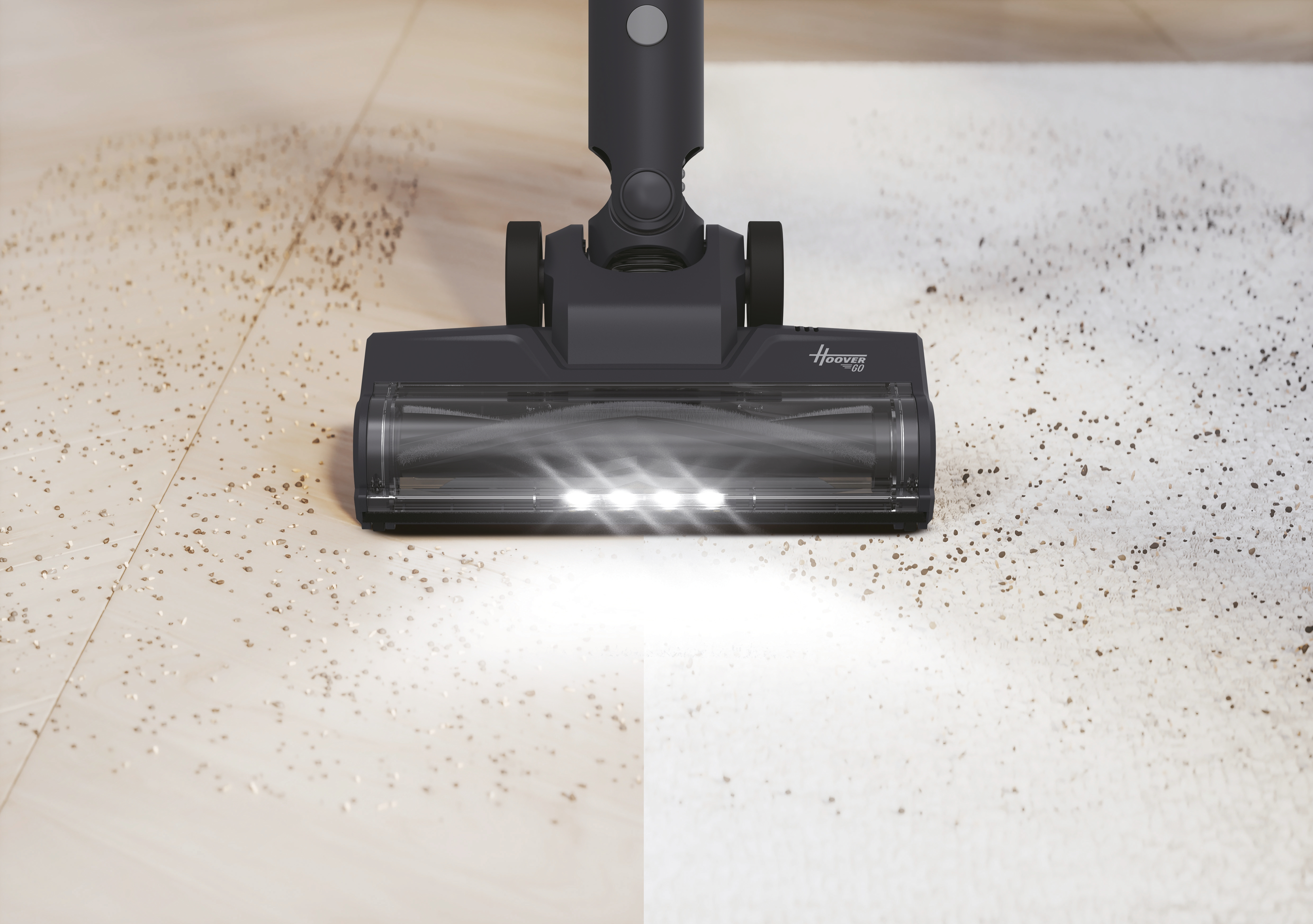 Un aspirateur noir nettoie un sol beige parsemé de débris. L'aspirateur a une lumière vive.