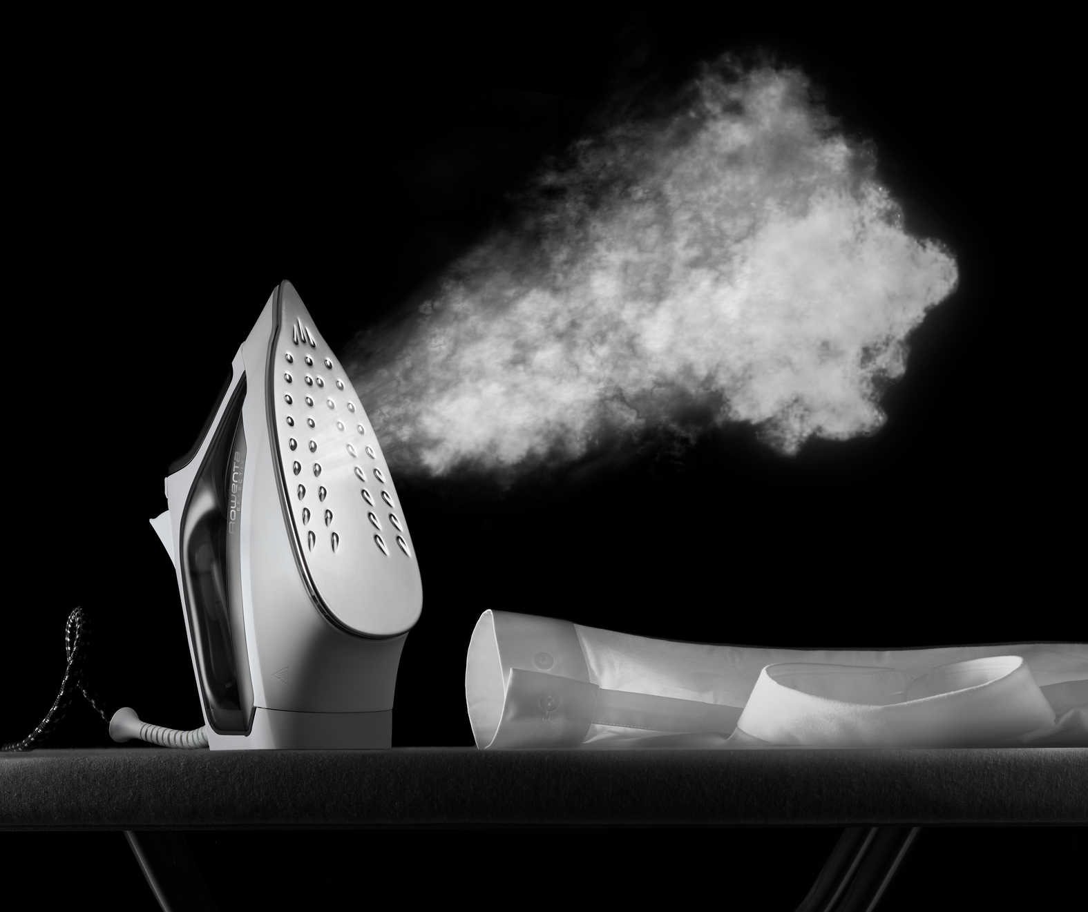 Białe żelazko parujące, biała koszula na desce do prasowania, na czarnym tle. Para unosi się z żelazka.