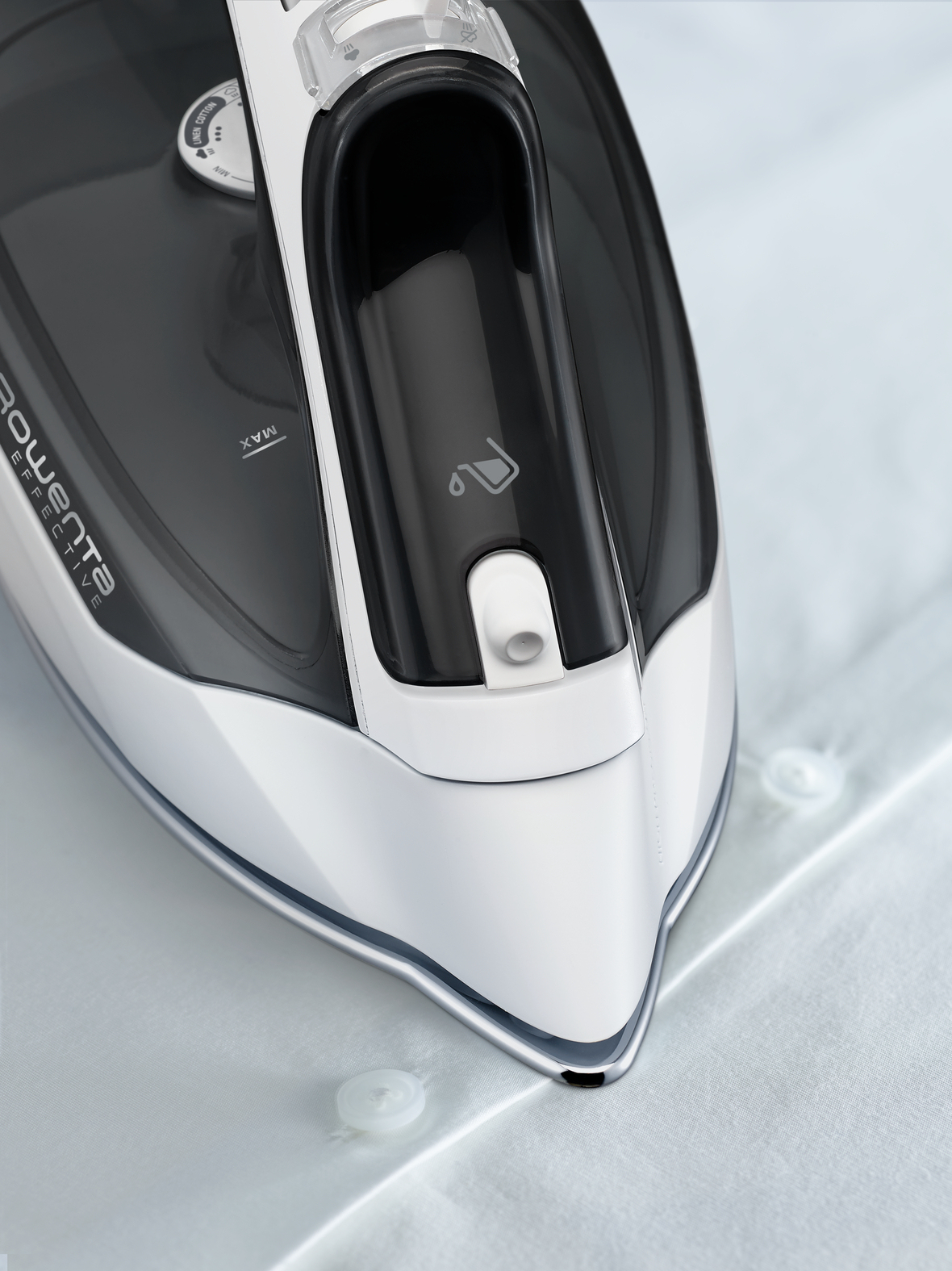 Zbliżenie żelazka Rowenta na białej koszuli. Żelazko jest czarne i srebrne. Na koszuli widoczne są guziki.