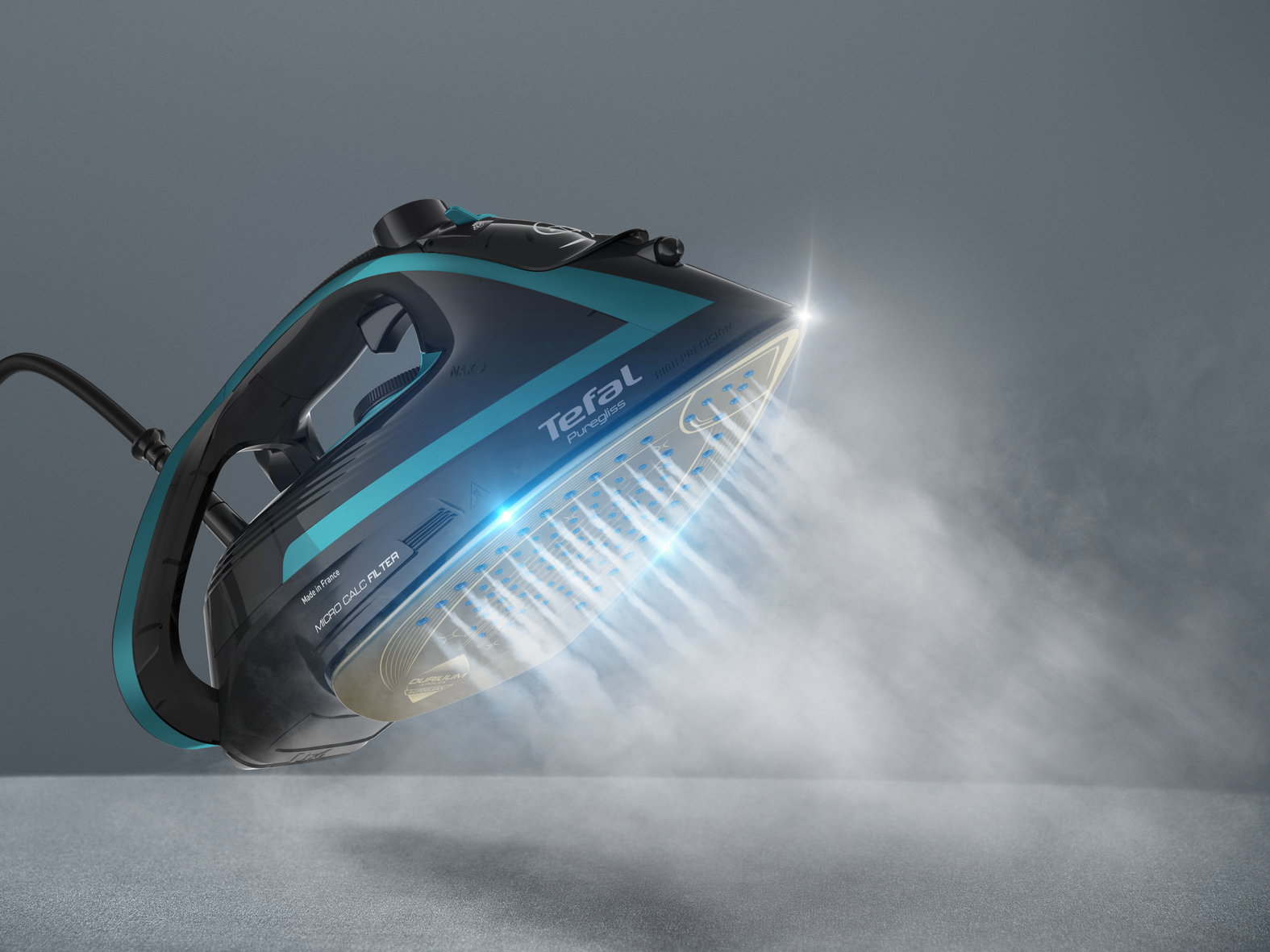 Żelazko Tefal, czarne i turkusowe, parujące. Żelazko w powietrzu, z parą wydobywającą się.