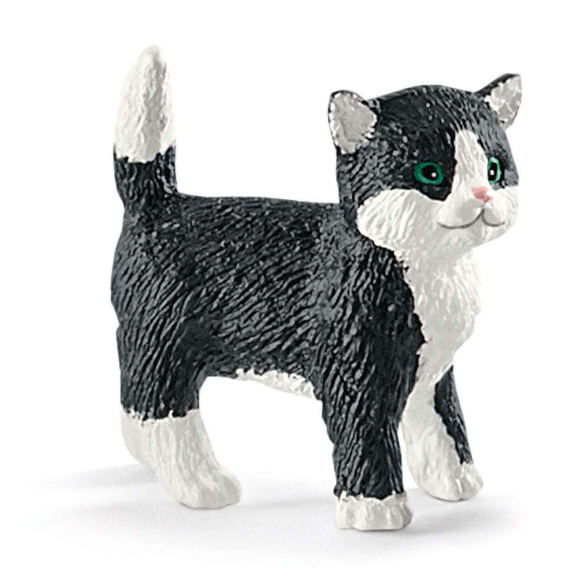 Eine Spielzeugkatze, schwarz und weiß, steht auf einer weißen Oberfläche. Sie hat grüne Augen und eine rosa Nase. Der Schwanz ist oben.
