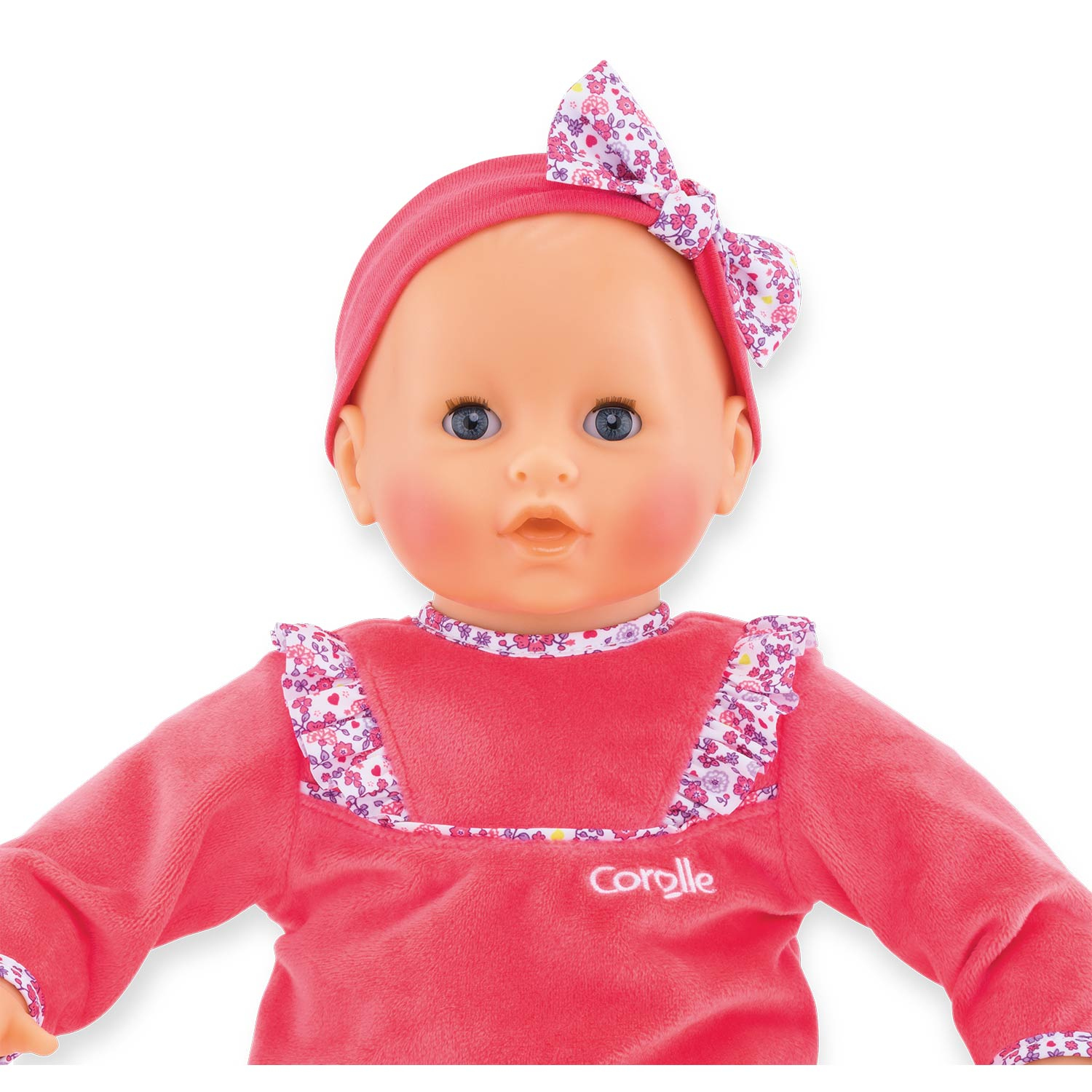 Eine Babypuppe mit blauen Augen, die ein rosa Stirnband und Kleid trägt. Das Kleid hat florale Details. Die Puppe ist vor weißem Hintergrund zentriert.