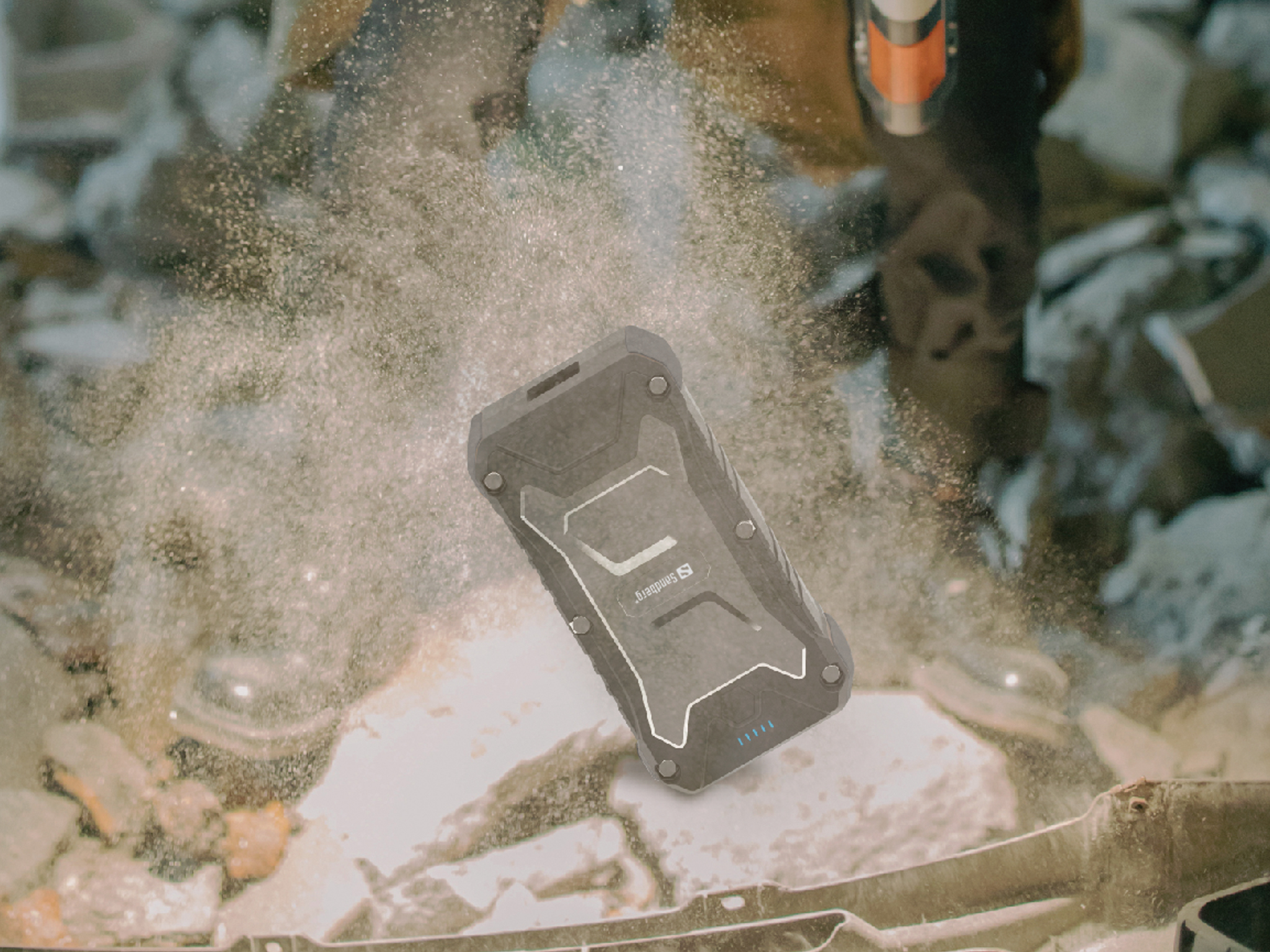 Eine robuste, schwarze Powerbank schwebt in der Luft. Staubpartikel umgeben sie. Im Hintergrund ist eine Person mit einem Werkzeug zu sehen.