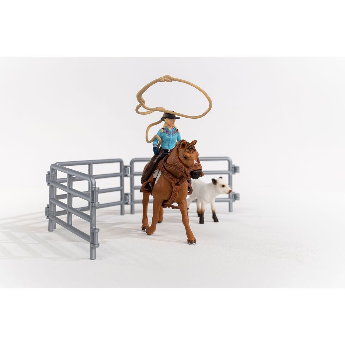 A toy cowboy on a brown horse with a rope, near a white calf and a gray fence, on a white background.