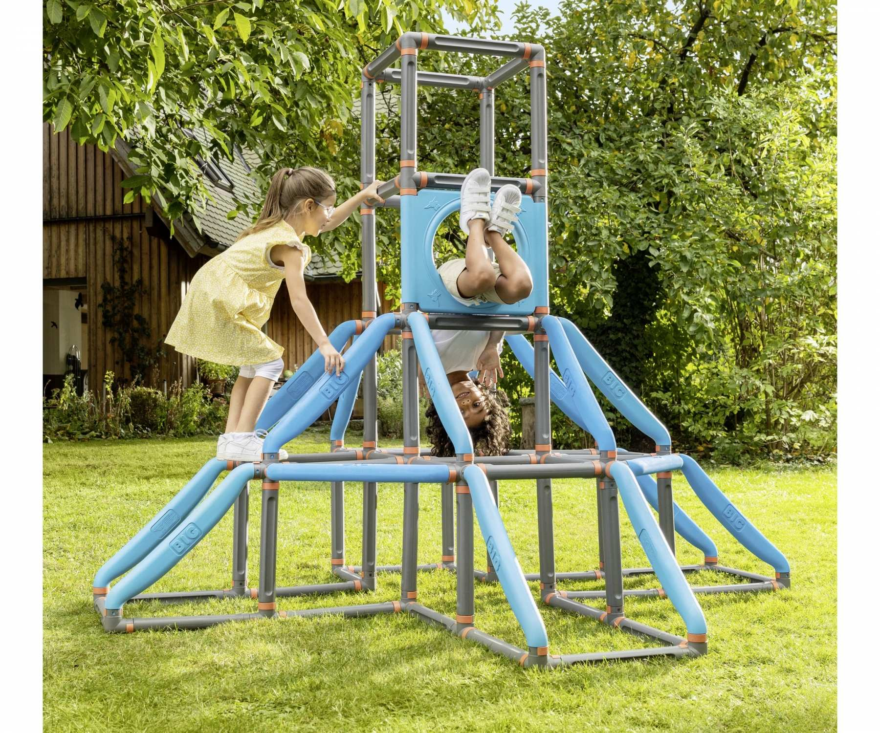 Zwei Kinder spielen auf einem blau-grauen Klettergerüst. Eines hängt kopfüber, das andere hilft.
