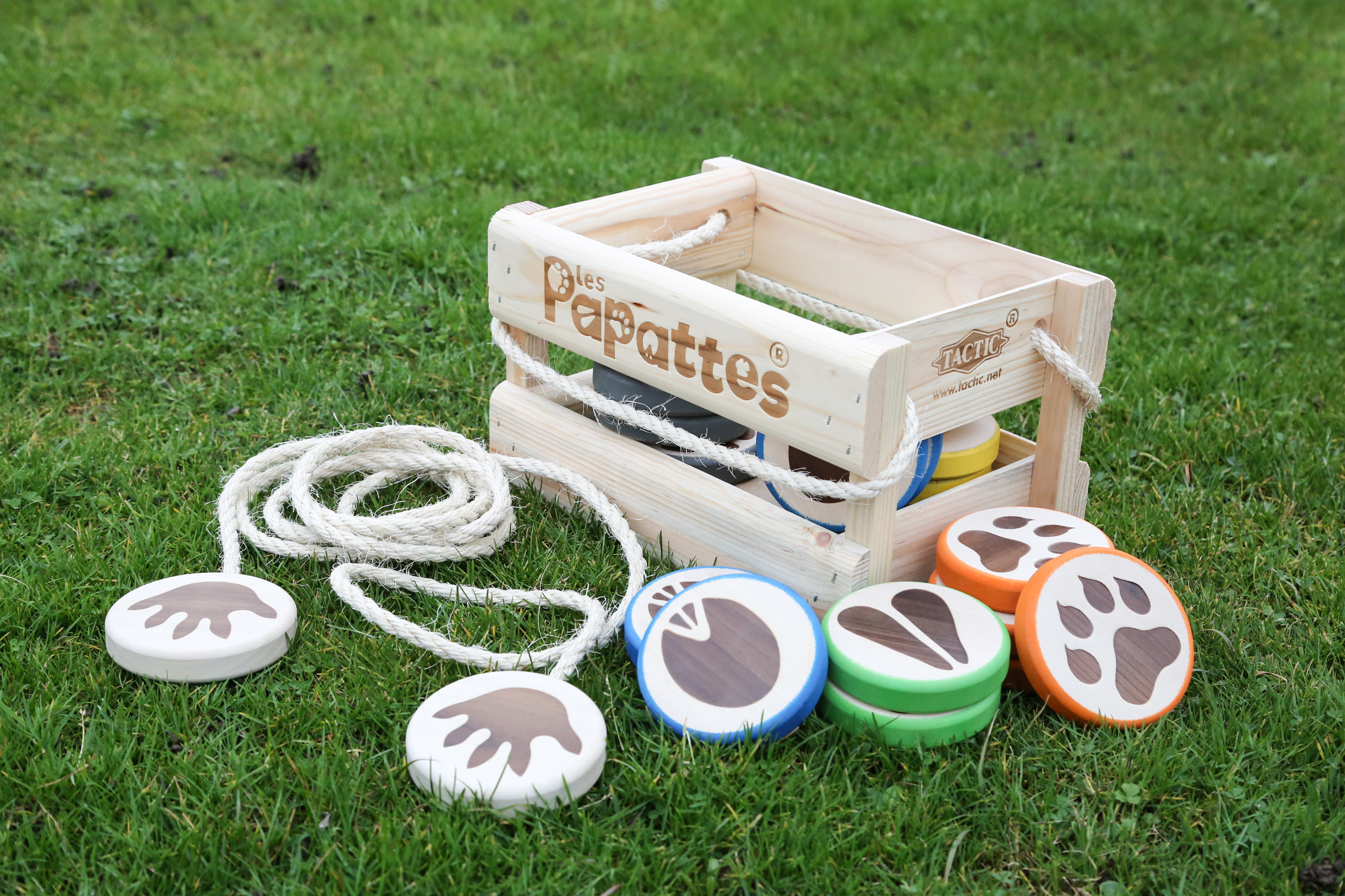 Un juego de madera sobre hierba. Incluye una caja, una cuerda y discos con huellas de patas en varios colores.