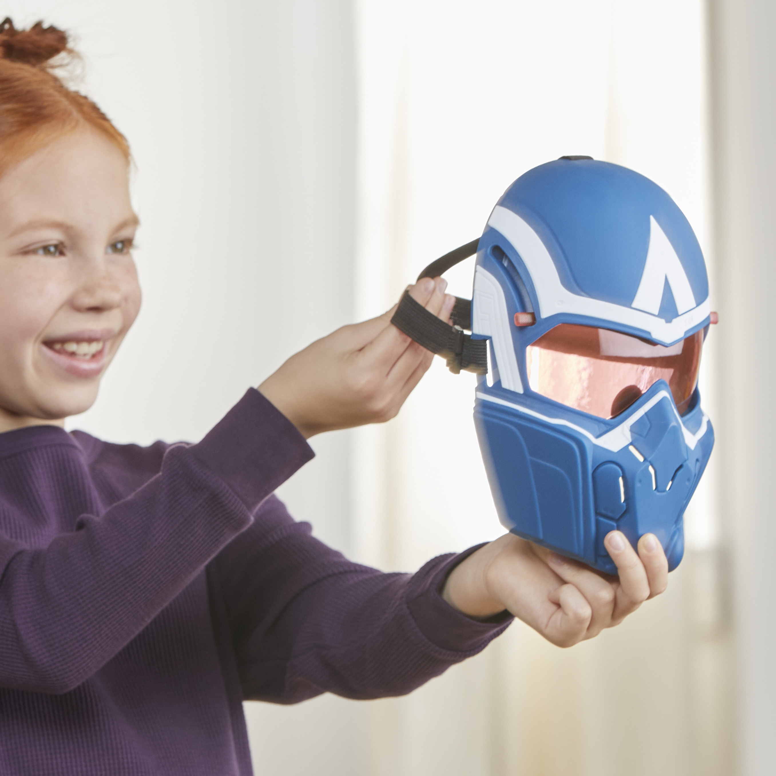 Una niña sostiene un casco azul y blanco con visera roja, sonriendo. Lleva una camisa morada.