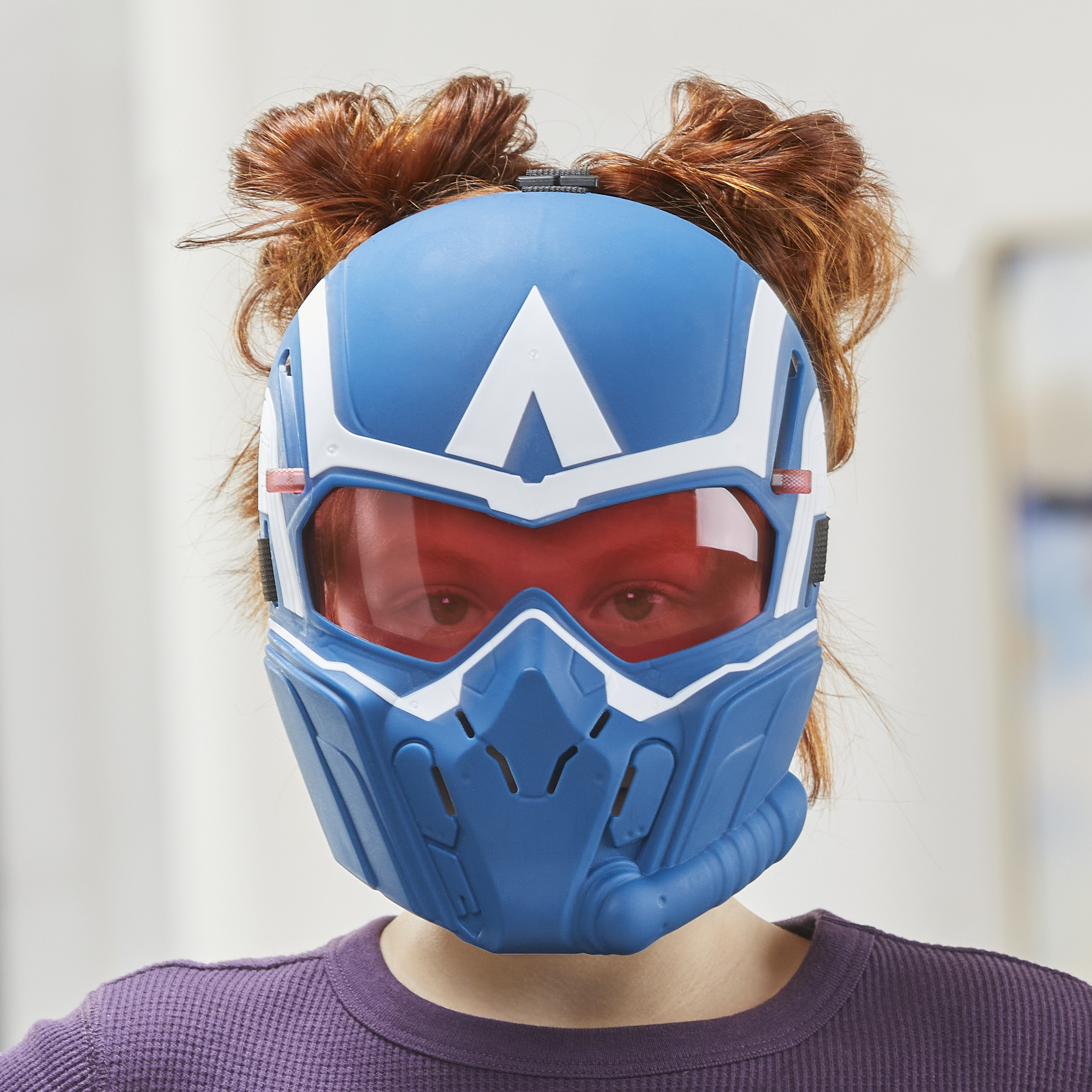 Una persona con un casco azul y blanco con visera roja. Se ve cabello rojo por encima del casco, y la persona lleva una camisa morada.