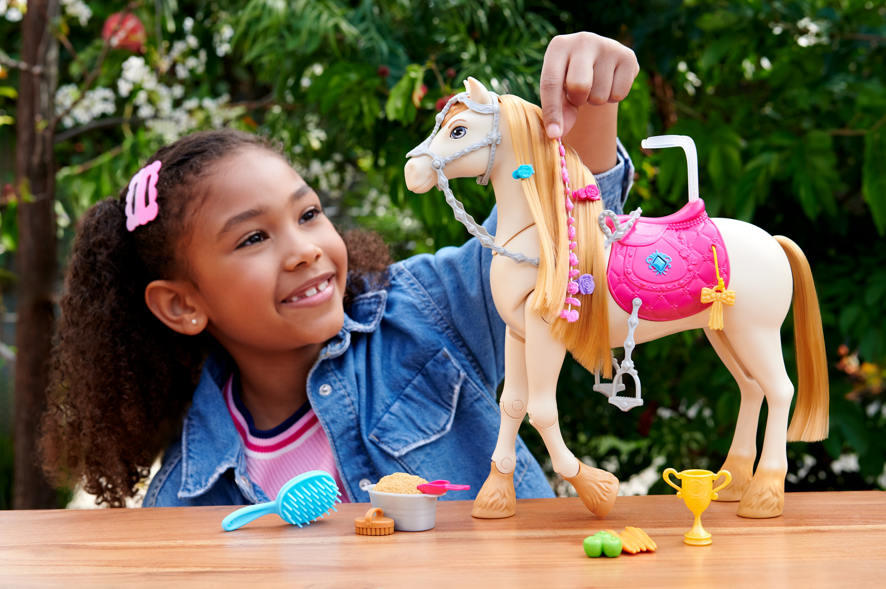 Ein lächelndes Mädchen hält ein Spielzeugpferd. Zubehör wie Bürste und Trophäe auf Holzoberfläche.