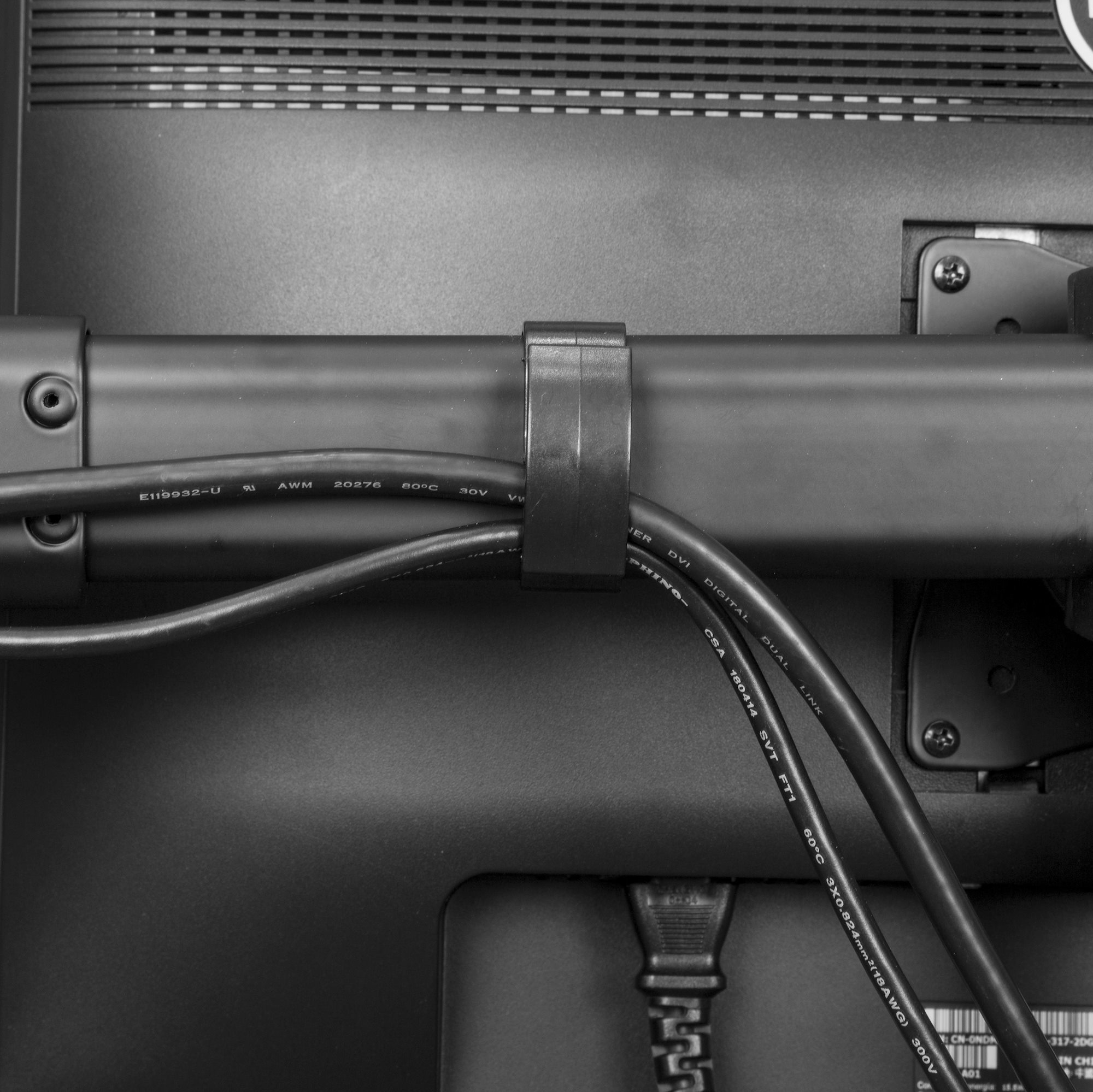 Primer plano de la parte trasera del monitor con cables. Un clip de plástico negro asegura los cables a una barra negra.