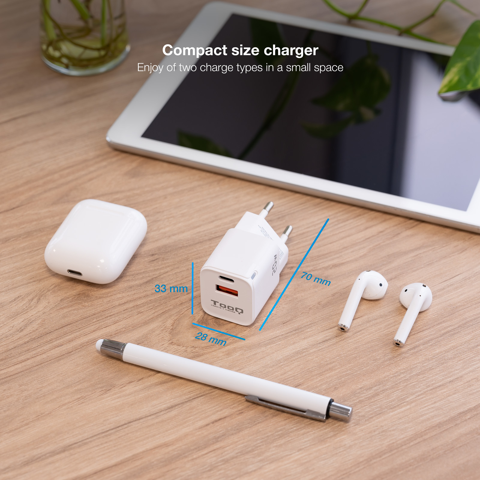 Cargador blanco, AirPods, bolígrafo y tableta en mesa de madera. Se muestran las dimensiones del cargador.
