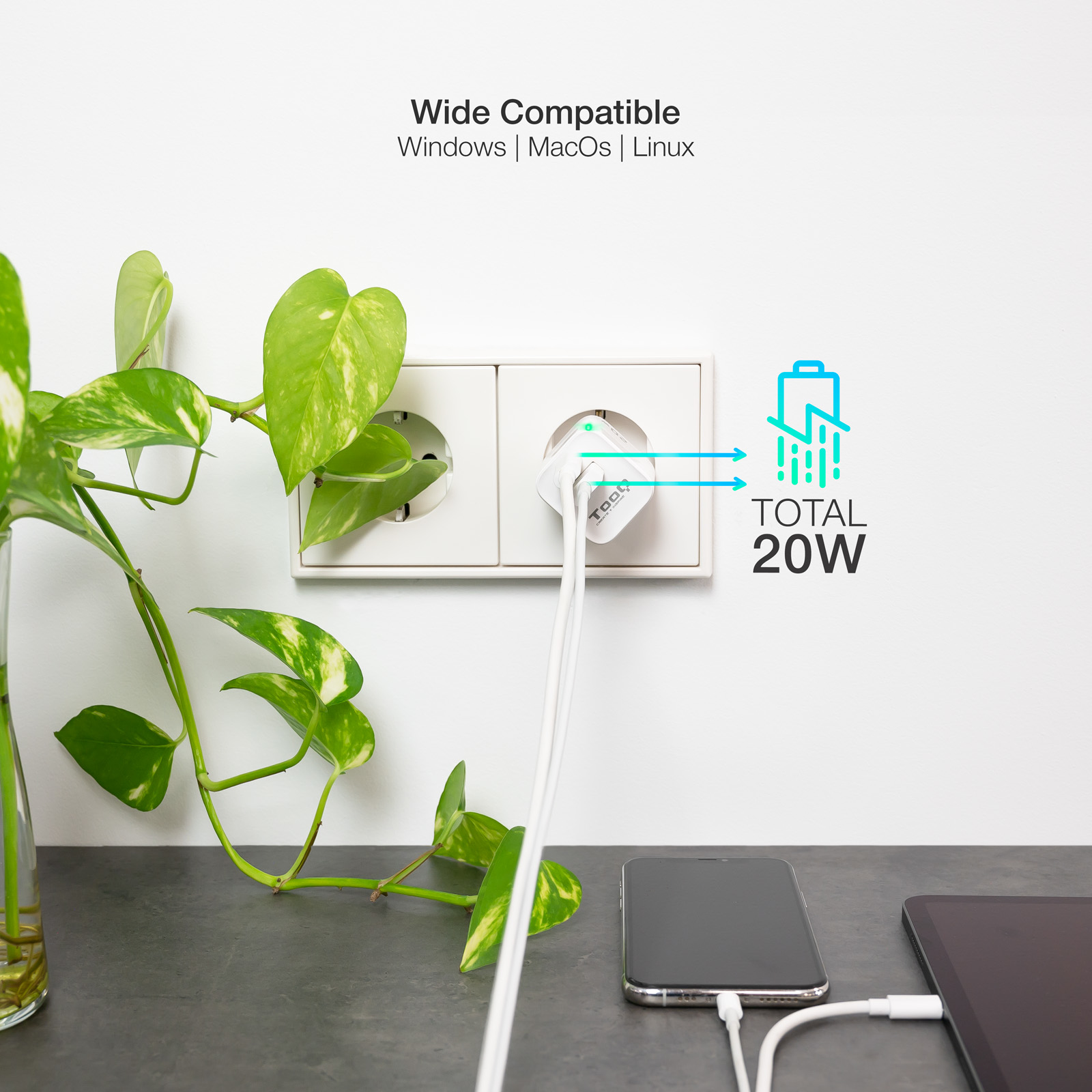 Un cargador blanco está enchufado a una toma de corriente, con cables conectados a un teléfono y una tableta. Una planta está en primer plano.