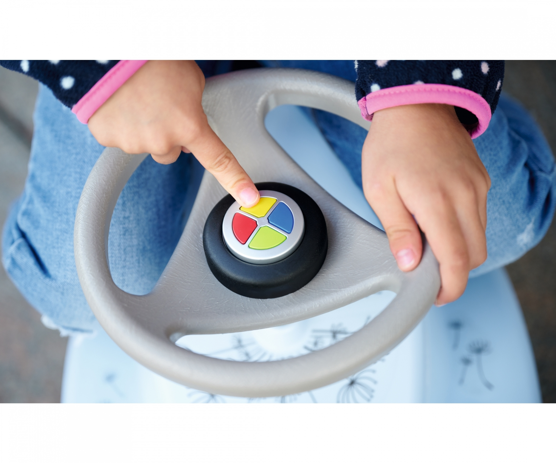 Kinderhände an einem Spielzeuglenkrad, Finger zeigt auf eine Taste mit farbigen Abschnitten: rot, gelb, grün und blau.