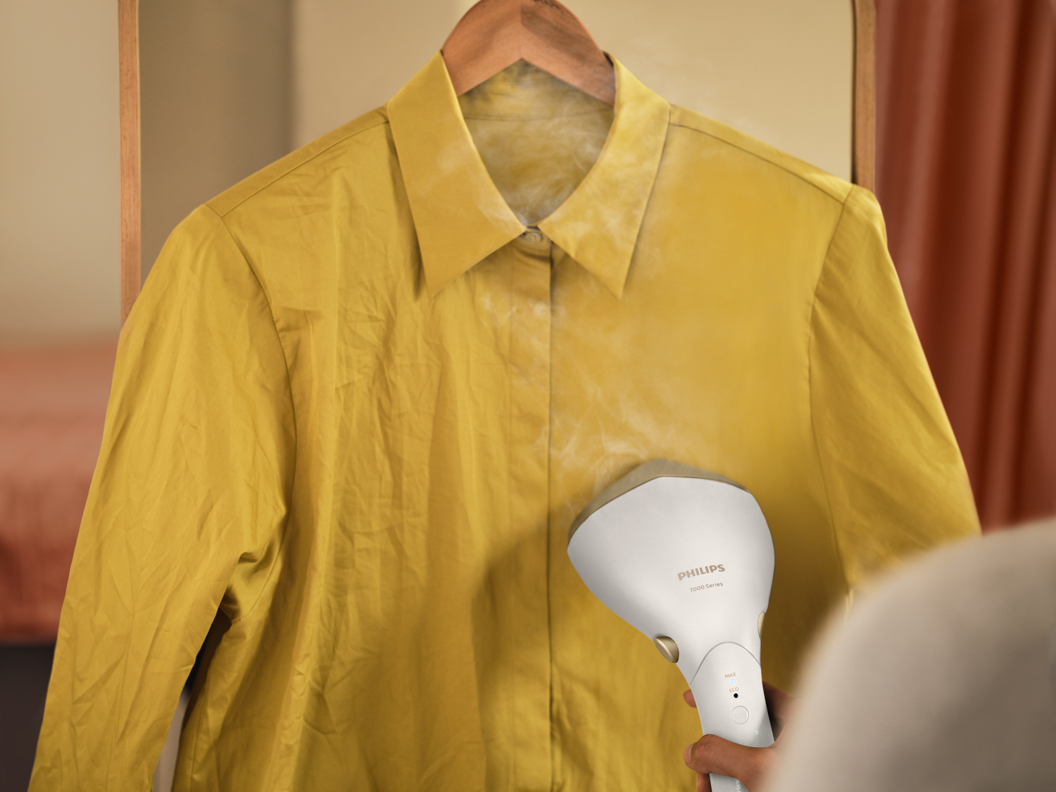 Ein gelbes Hemd wird mit einem weißen Steamer gedämpft. Das Hemd hängt an einem Holzkleiderbügel vor neutralem Hintergrund.