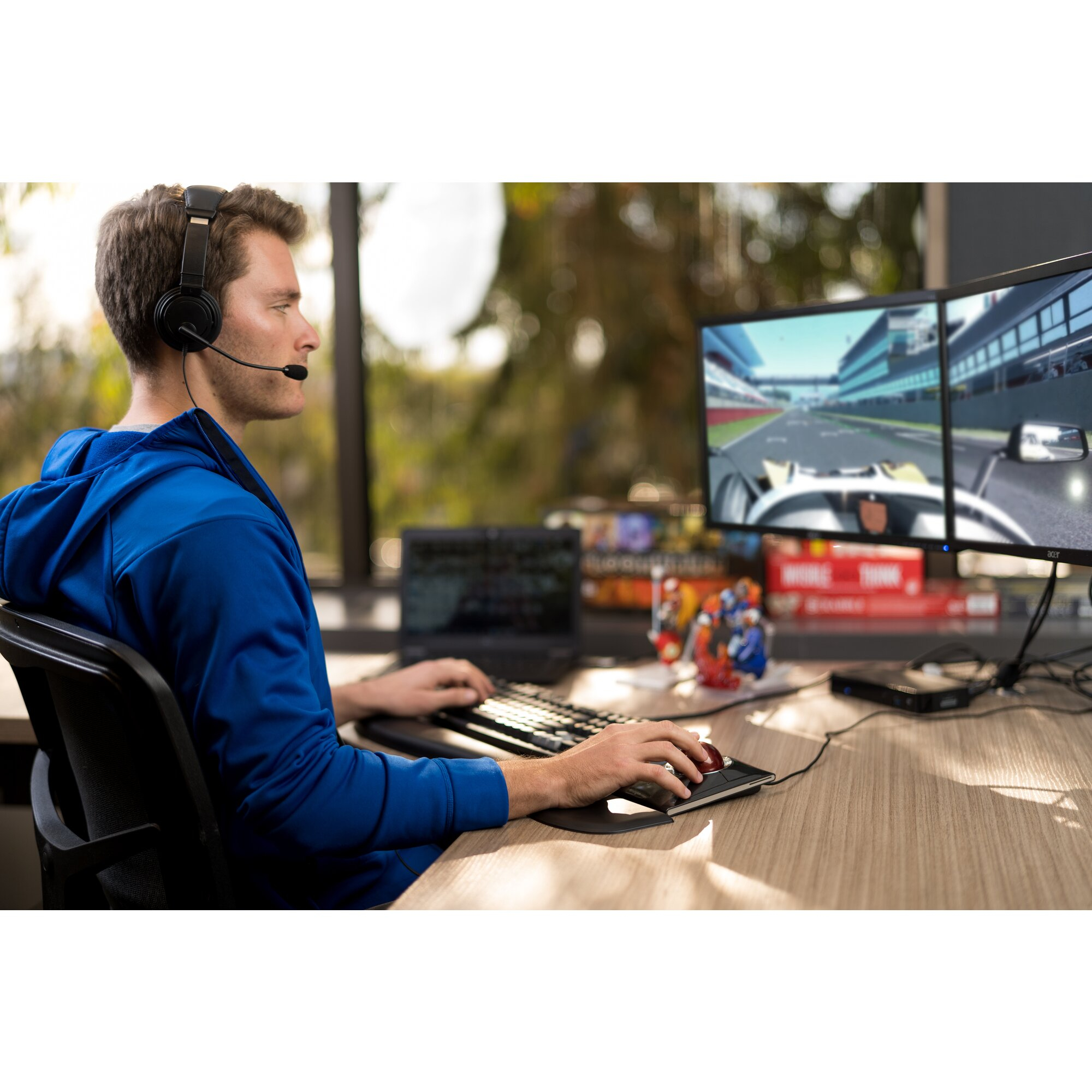 Hombre con auriculares jugando en una computadora con un juego de carreras en el monitor. Lleva una chaqueta azul.