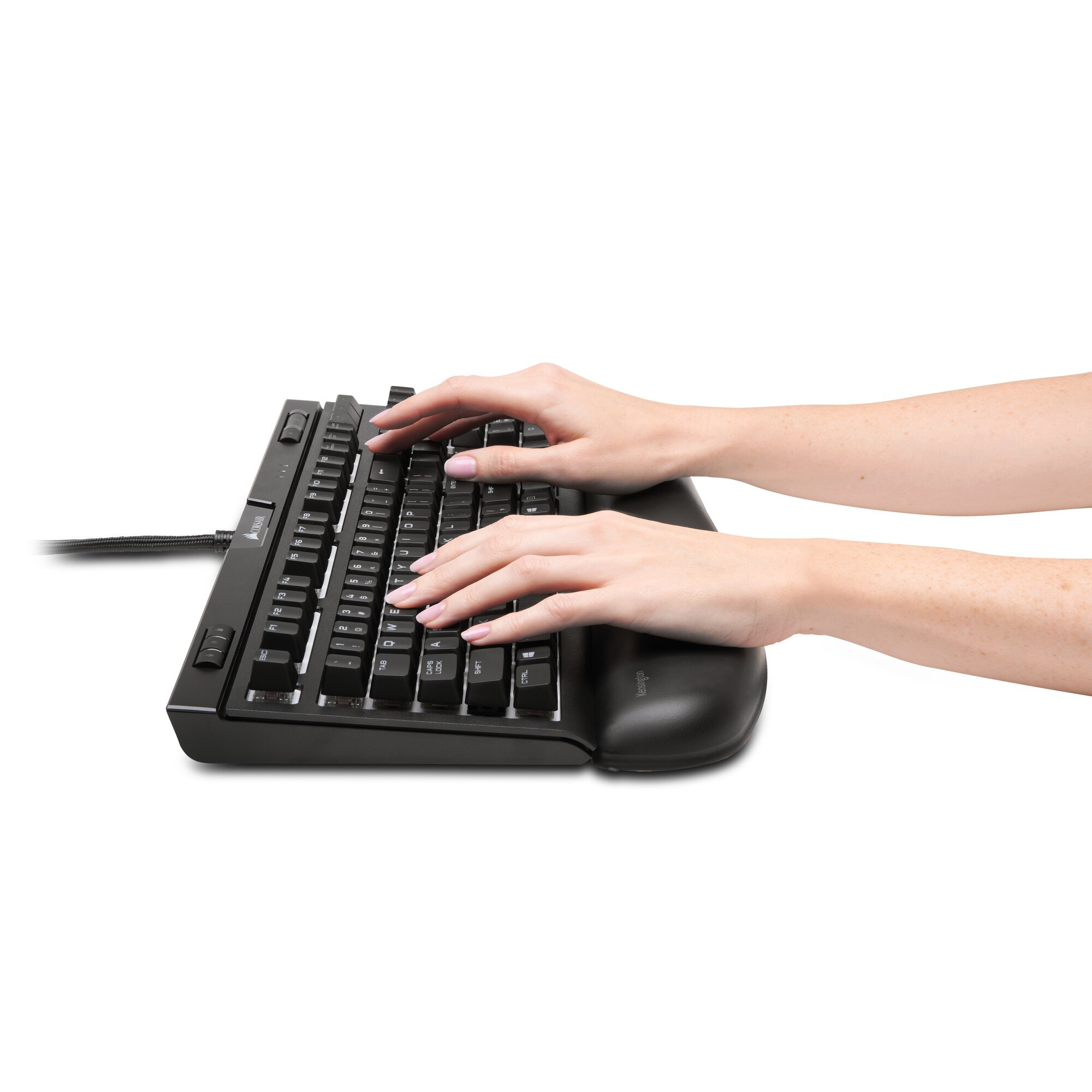 Manos tecleando en un teclado negro con reposamuñecas. Teclas visibles. El fondo es blanco.
